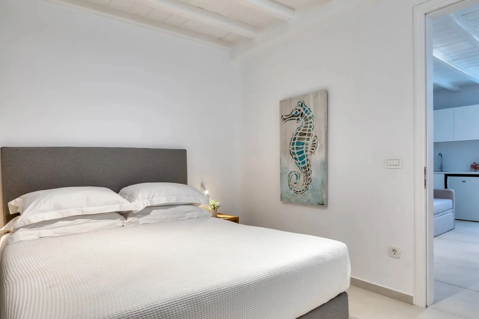 A bright bedroom with a neatly made bed and seahorse artwork on the wall.