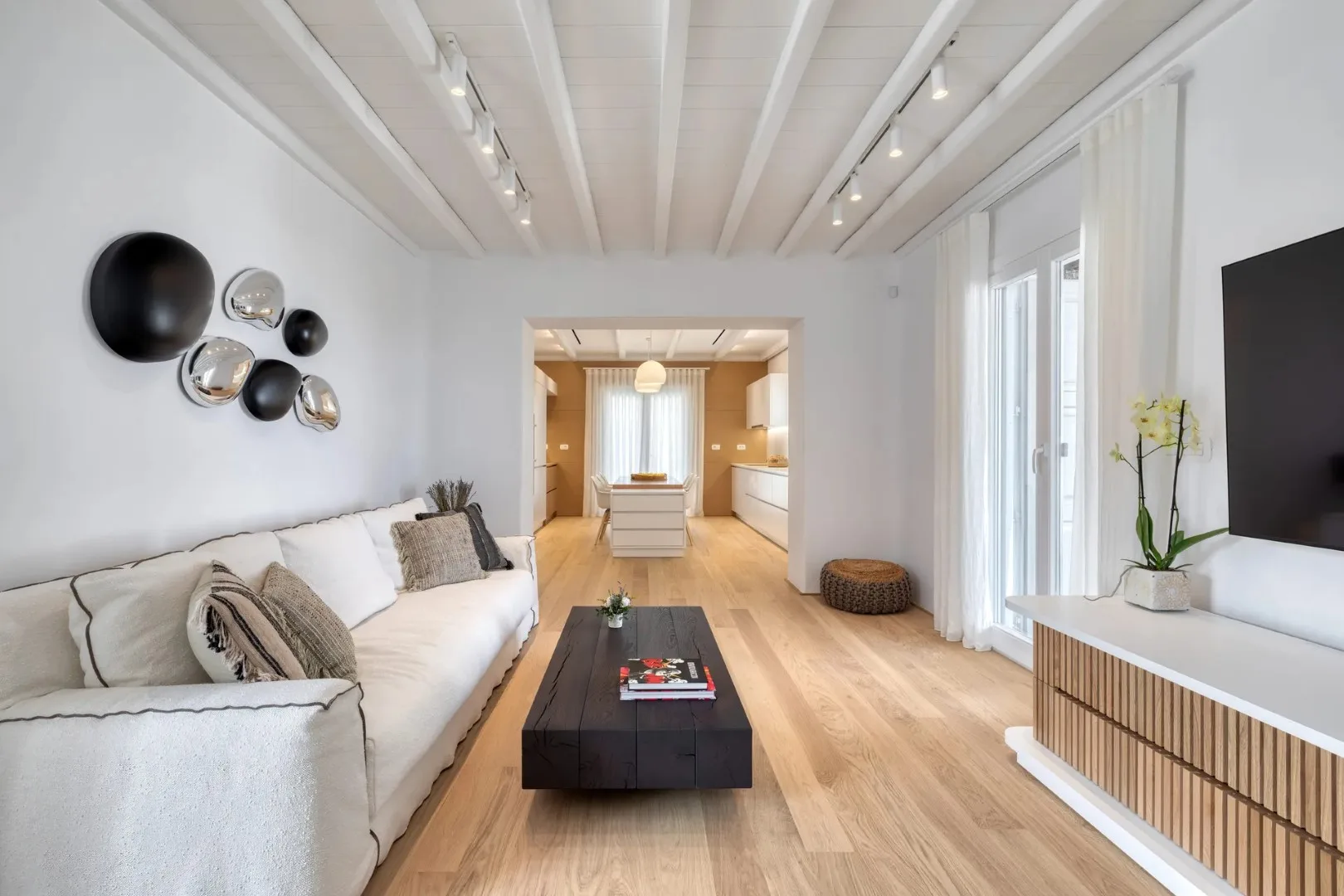 A bright living room with seating, a coffee table, and an open kitchen beyond.