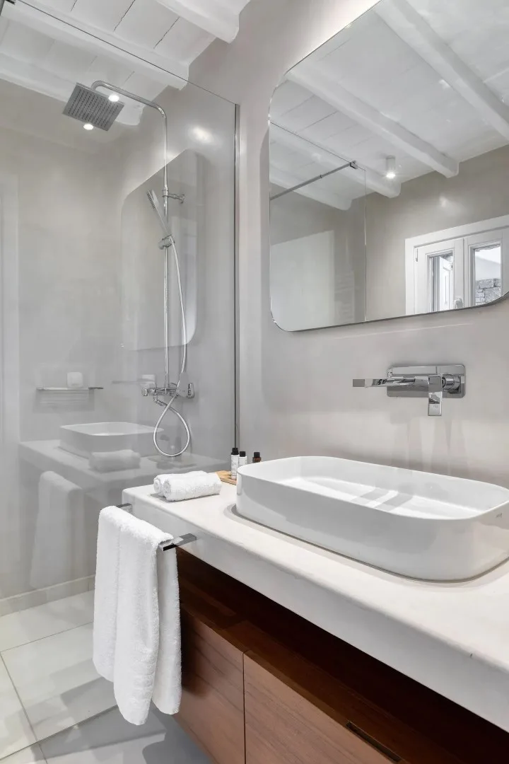 A bright bathroom with a large mirror, wall-mounted shower, and countertop basin.