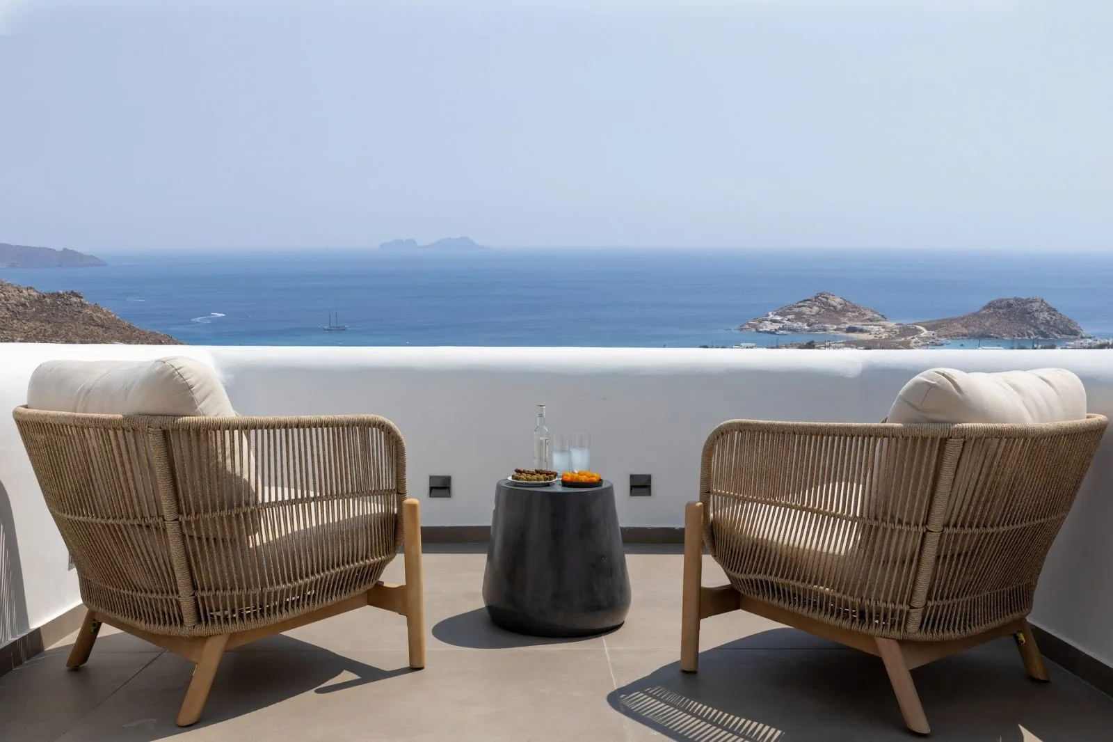 A terrace seating area faces the sea, with two chairs beside a small table.