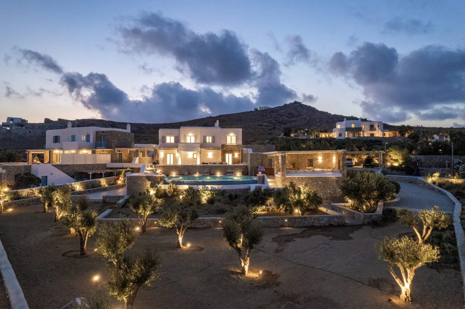 A landscaped property is illuminated at dusk beneath a cloudy sky.