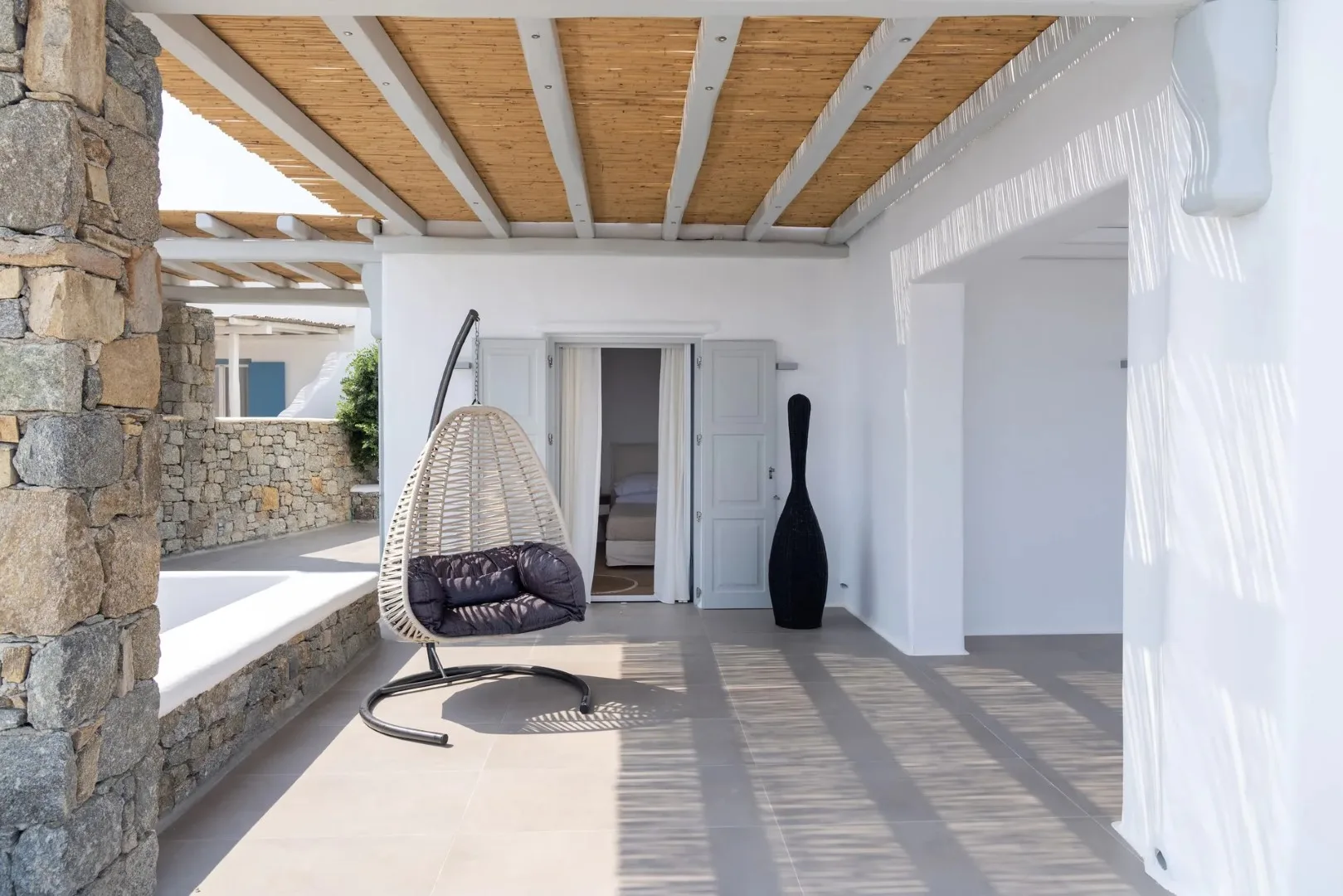 A covered patio with a hanging seat and stone walls.