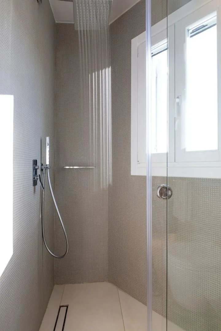 A tiled bathroom shower with a handheld showerhead and a window.