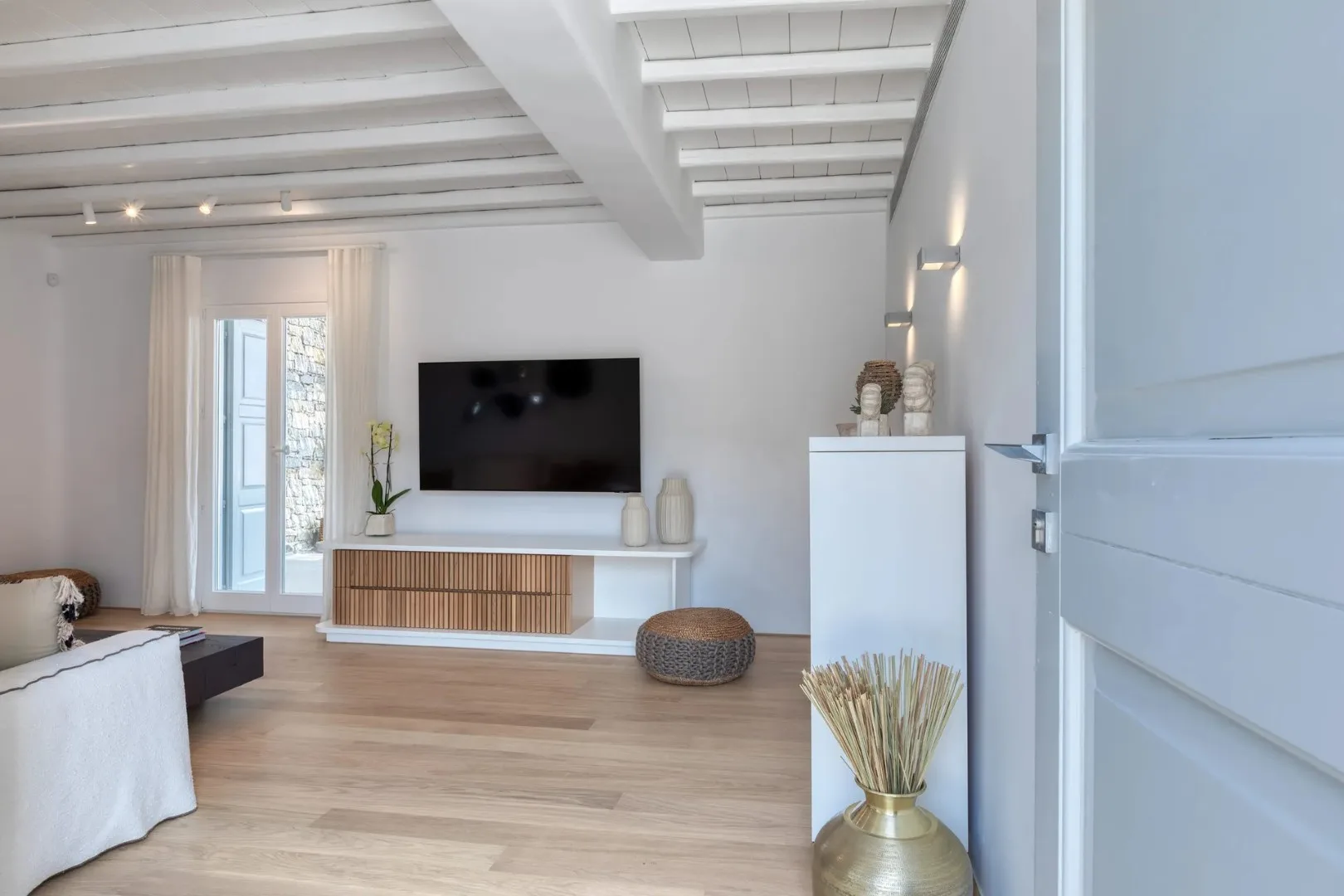 A bright living room with a television on a low console and light wood flooring.