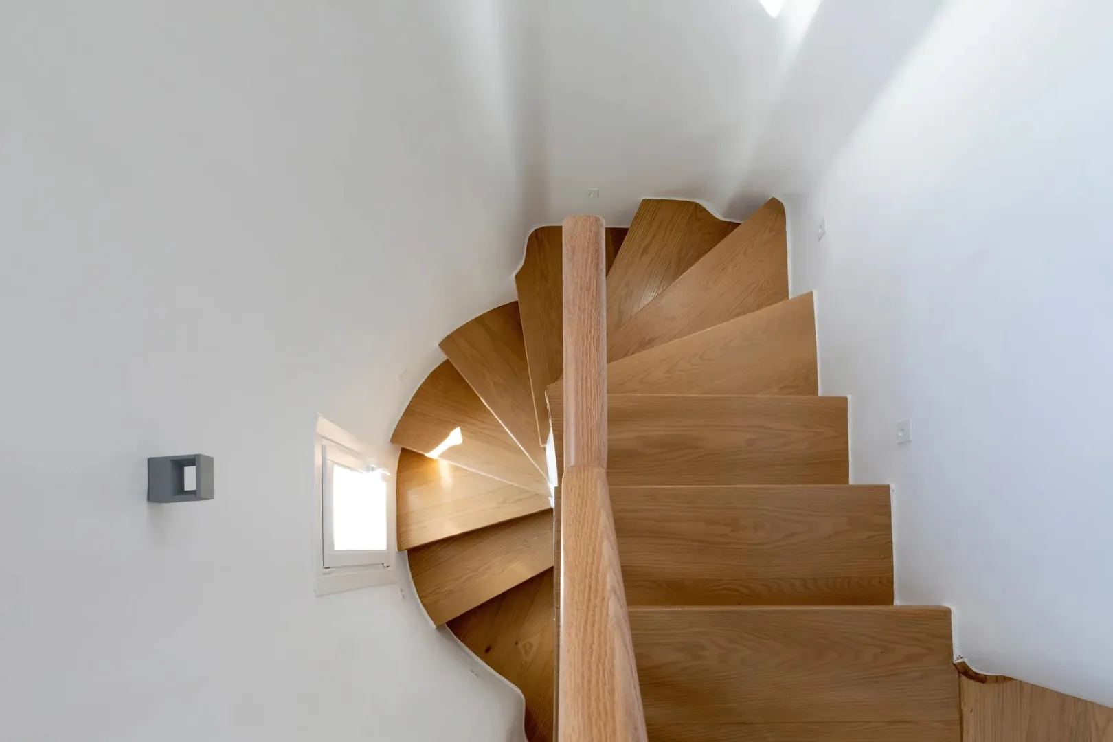 A wooden spiral staircase rises through a bright white interior.