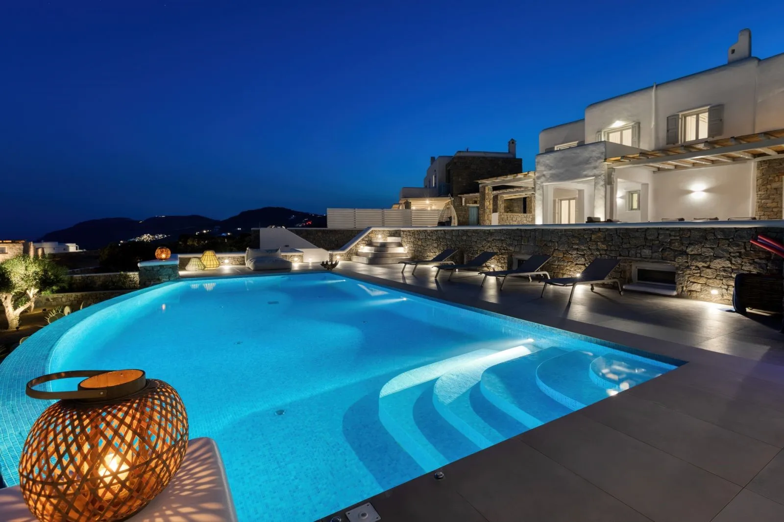 An illuminated outdoor swimming pool beside a modern building at dusk.