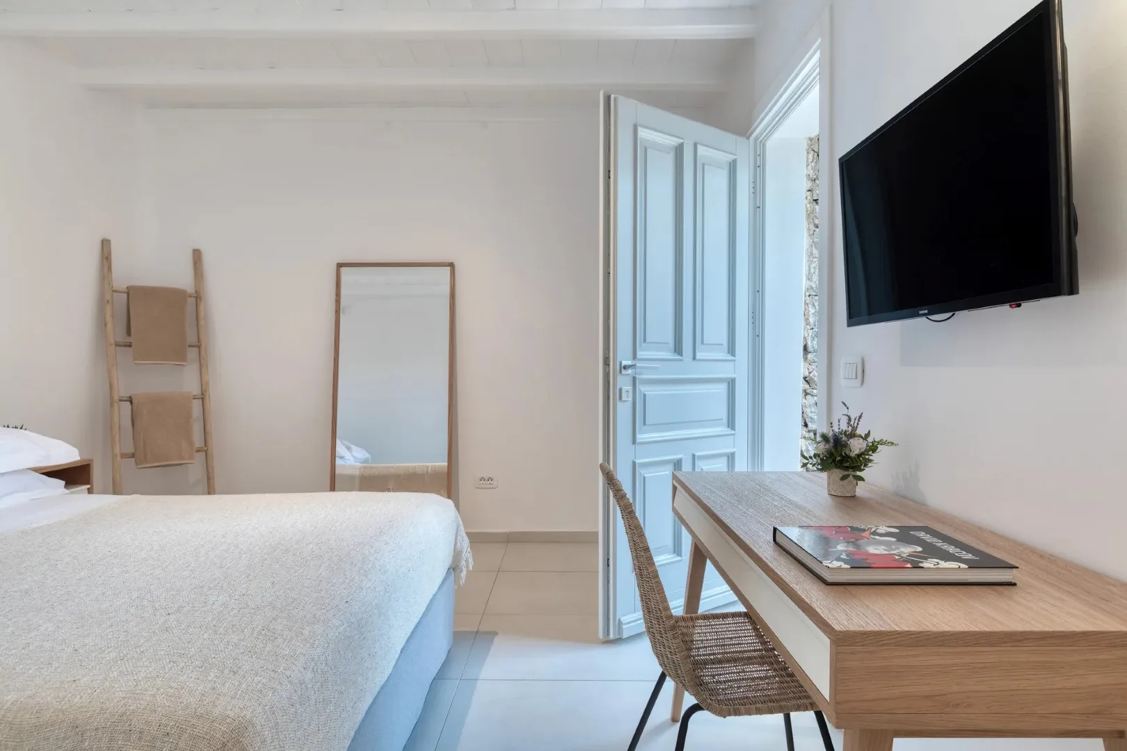 A bright bedroom with a bed, a wooden desk, and a wall-mounted television.