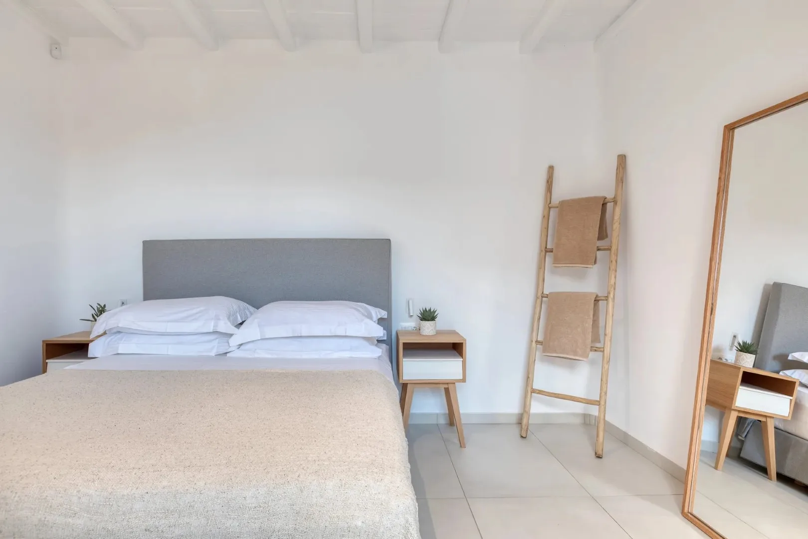 A bright bedroom with a neatly made bed and a ladder-style towel rack.