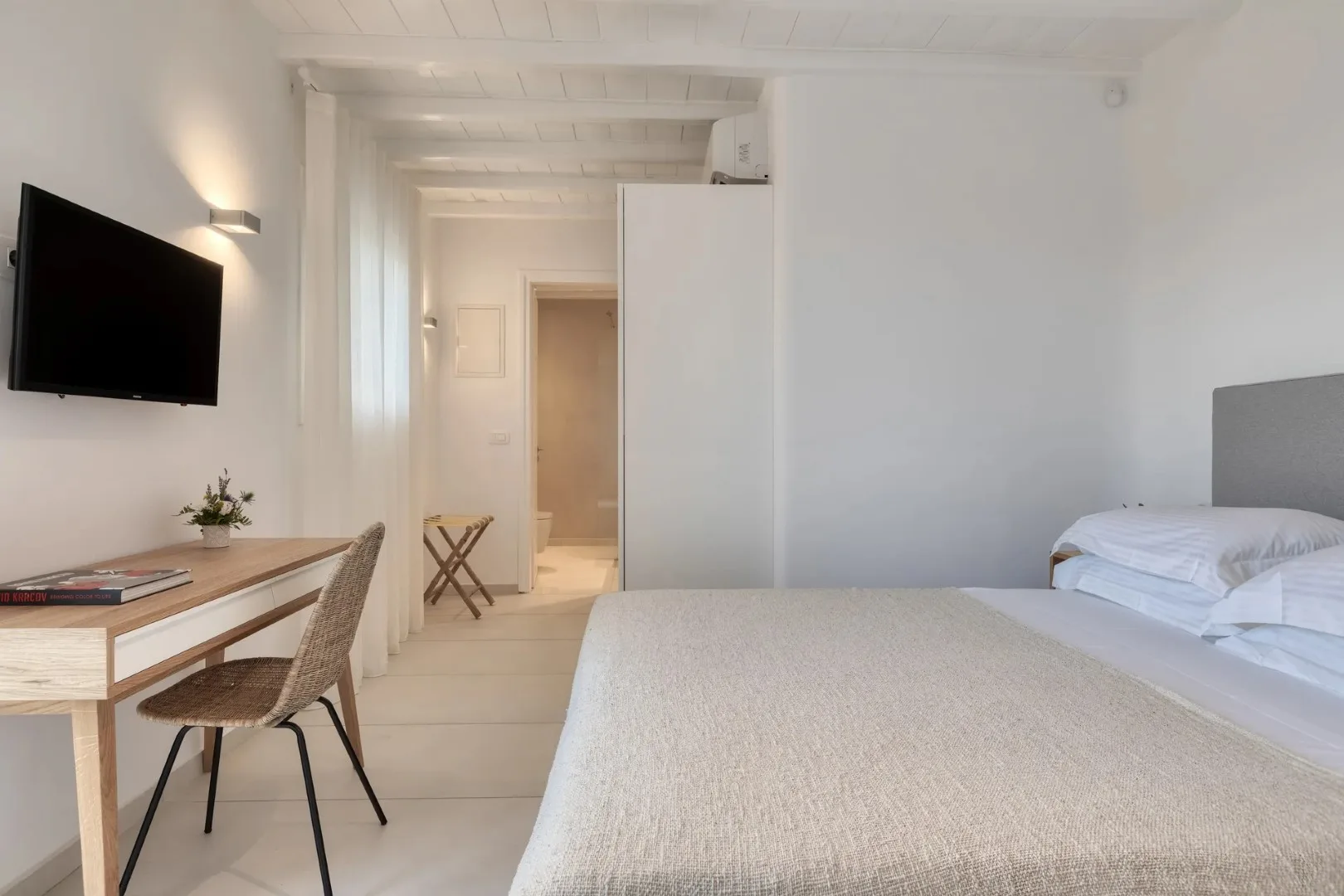 A bright bedroom with a bed, desk, and television on the wall.