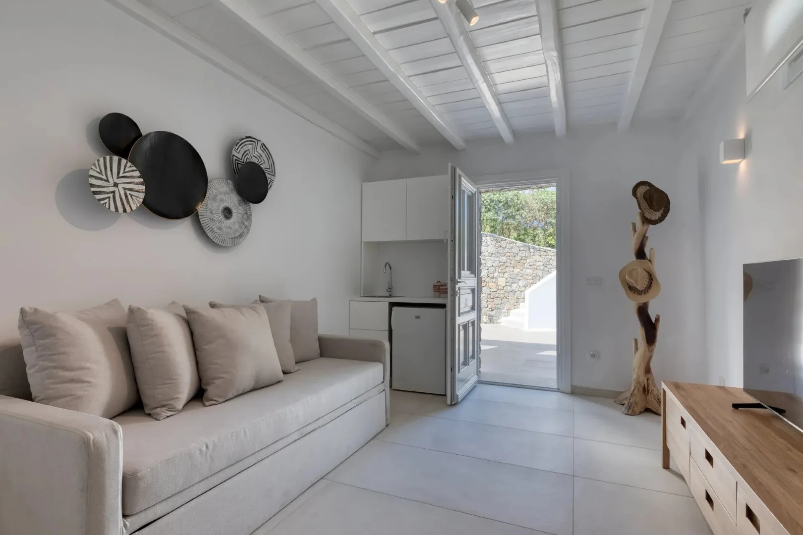 A bright living room with pale seating and an open door to an outdoor area.
