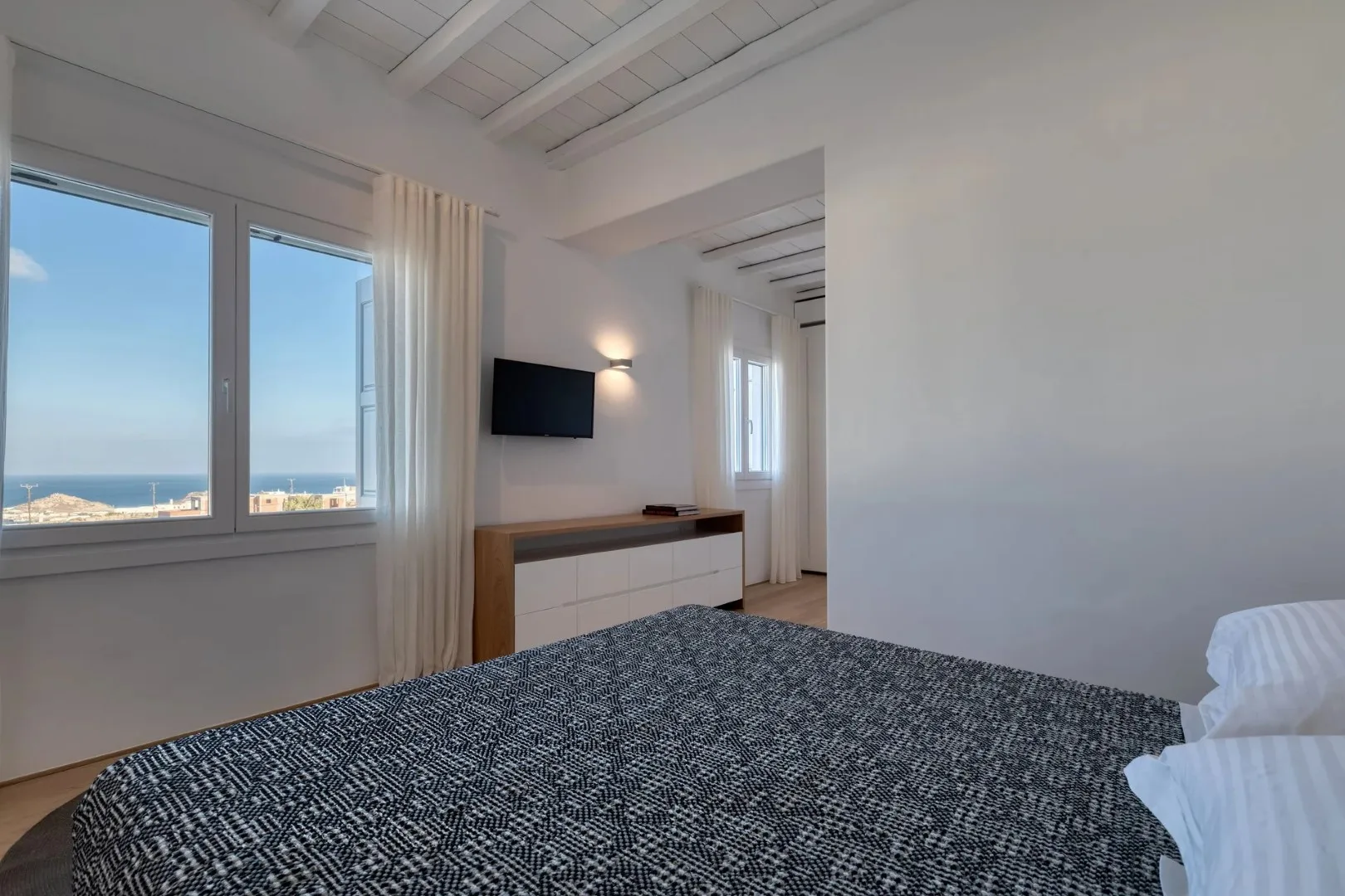 A bedroom with a bed, television, and windows overlooking the sea.