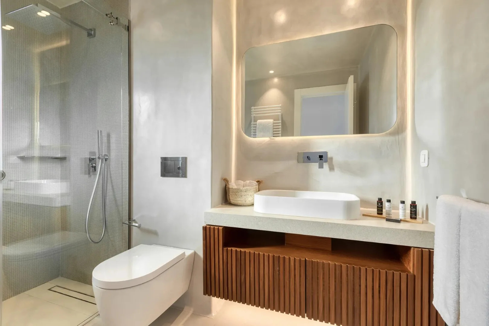 A modern bathroom with a glass shower, toilet, and vanity beneath a large mirror.
