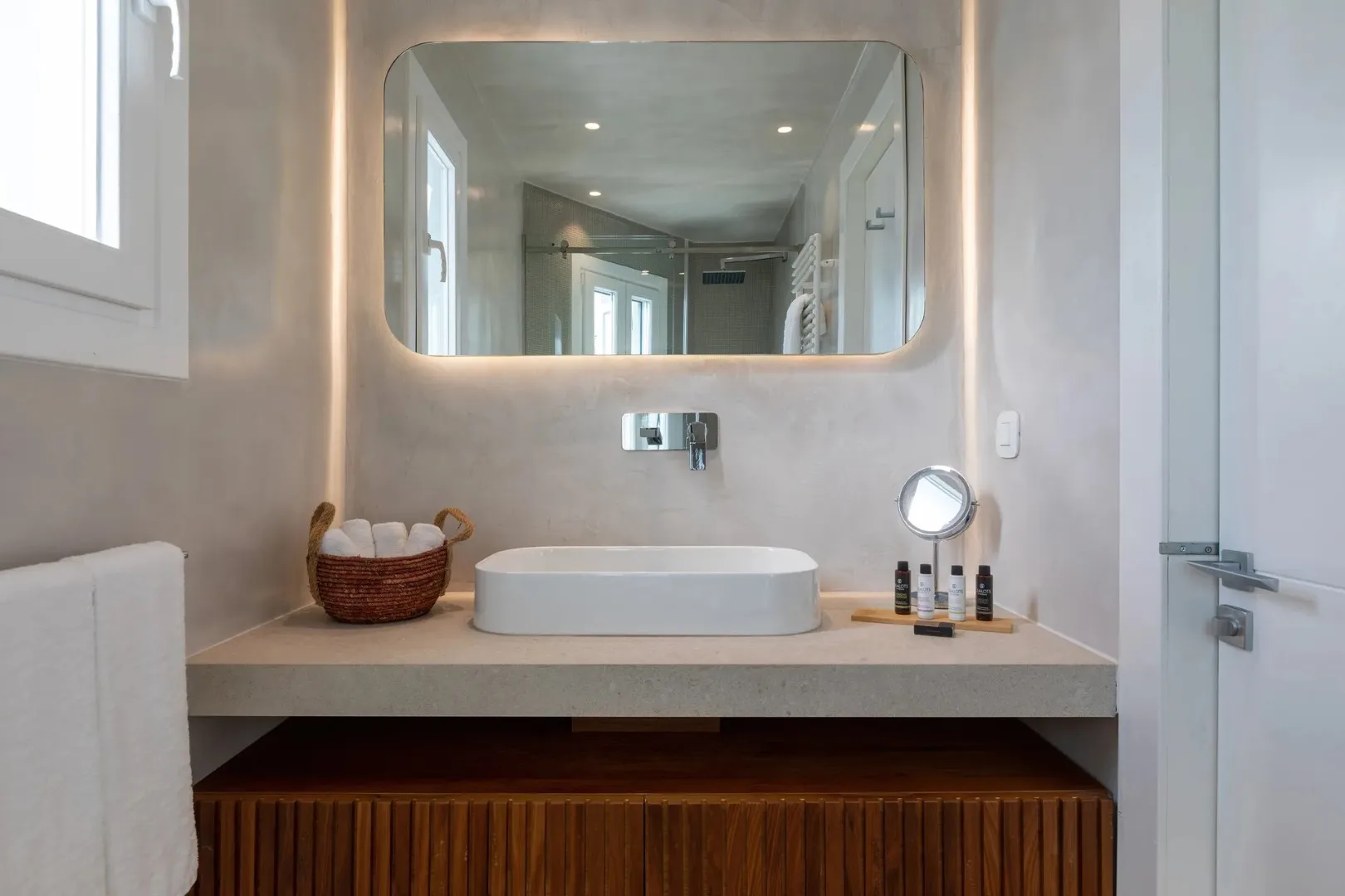 A bathroom vanity with a vessel sink sits beneath a large illuminated mirror.