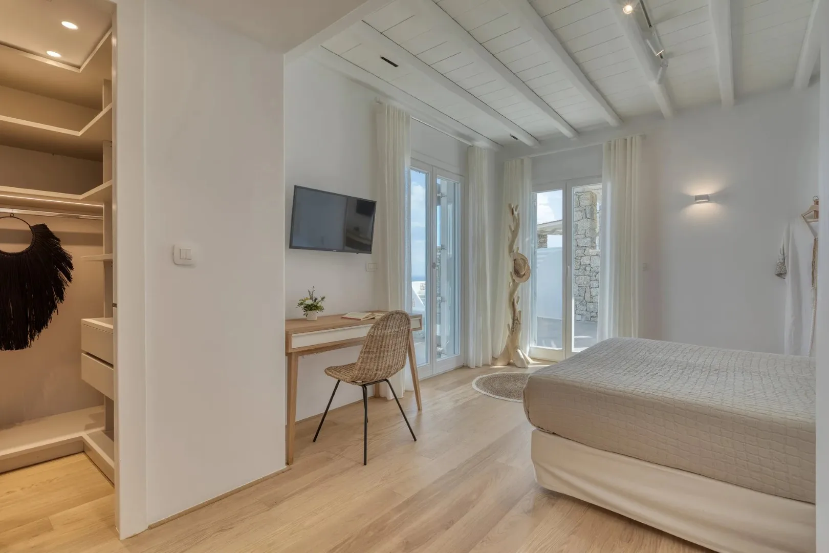 A bright bedroom with a bed, desk, and tall windows.