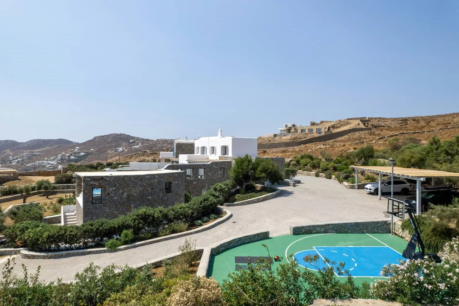 A hillside property with white buildings, a paved courtyard, and a small sports court.