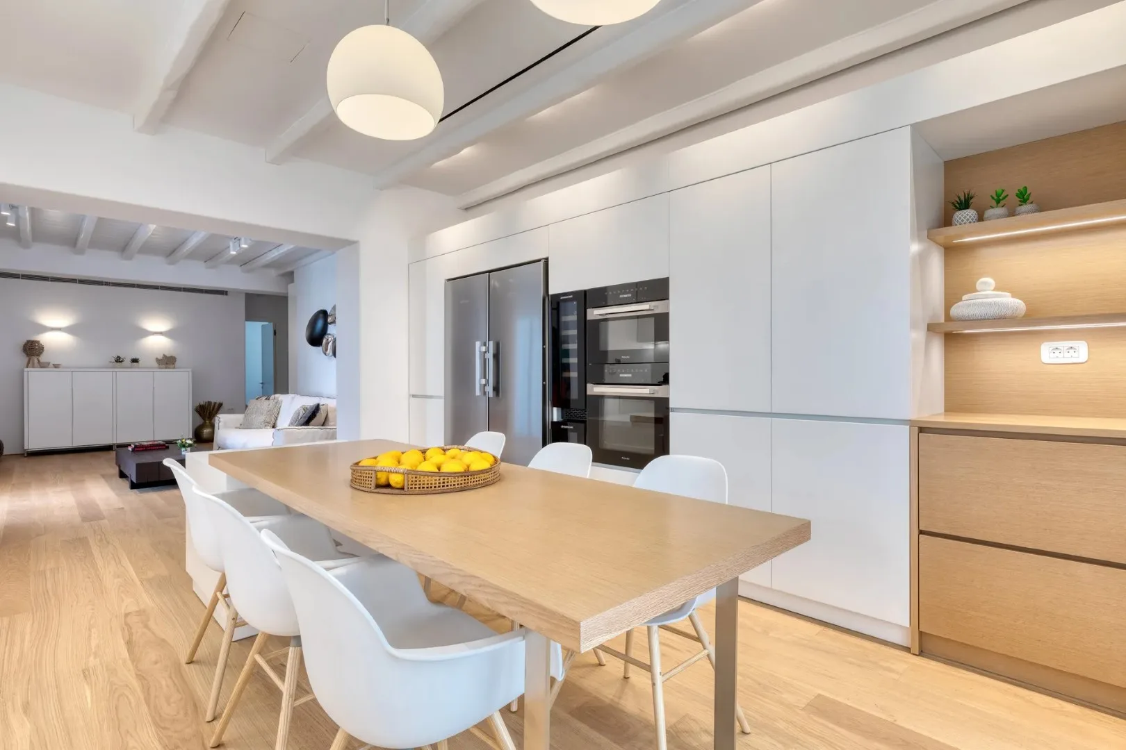 A bright open-plan dining area with a wooden table and modern kitchen.