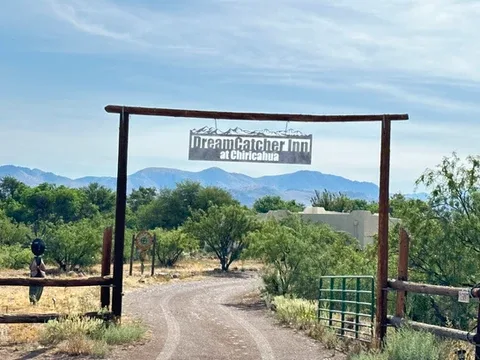 Representative hotel space: A gravel driveway passes beneath a wooden entrance sign, with trees and mountains beyond.