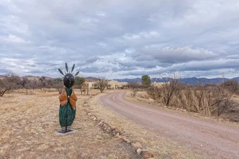 Representative hotel space: A rural dirt road winds past a standing sculpture beneath a cloudy sky.
