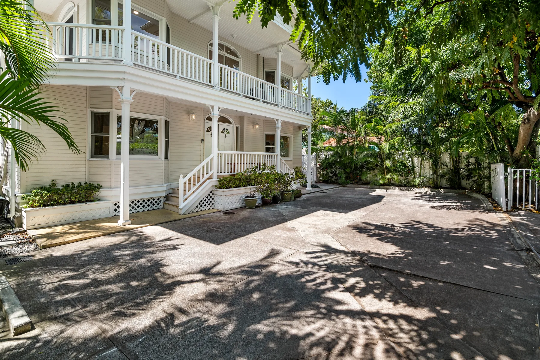 A white two-story building stands beside a paved driveway shaded by trees.