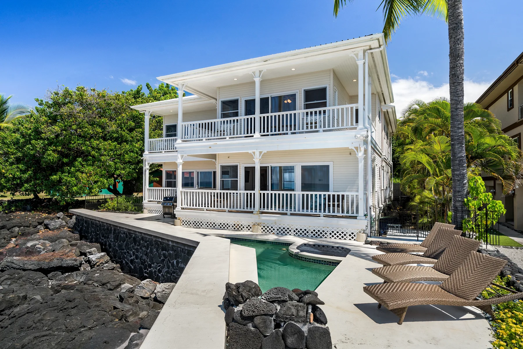 A white two-story house with balconies overlooks a small pool and outdoor seating.