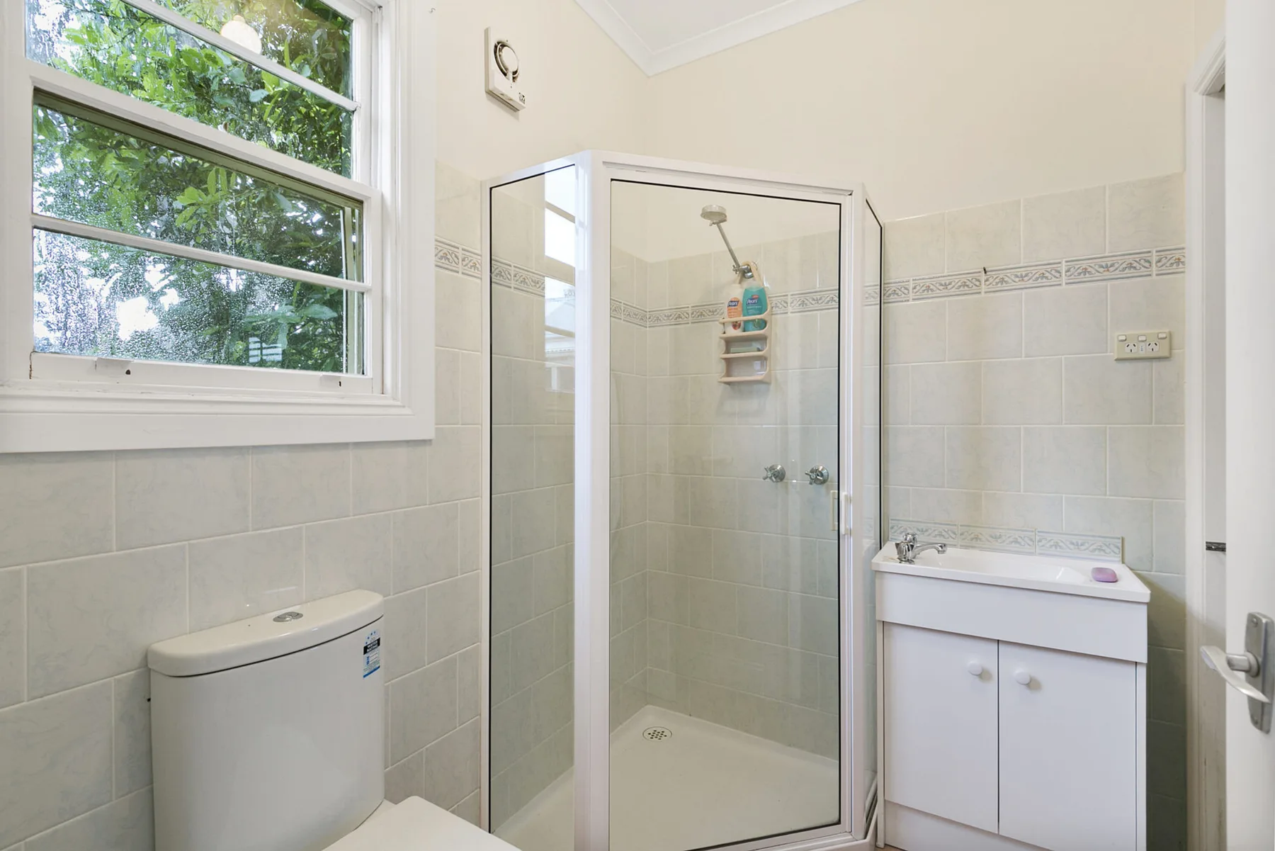 A bright bathroom with a glass shower, sink cabinet, and window.