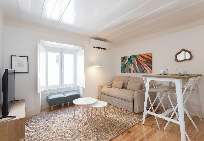 Una sala luminosa con un sofá, mesas pequeñas y un comedor junto a la ventana.
