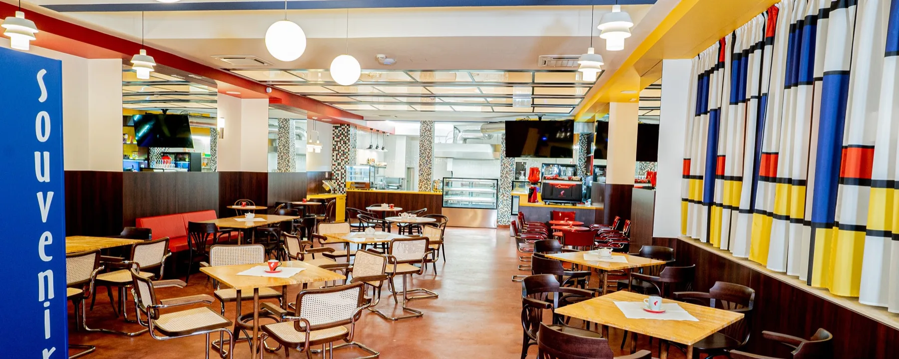 Espacio representativo del hotel: Comedor de restaurante con mesas y sillas junto a cortinas coloridas.