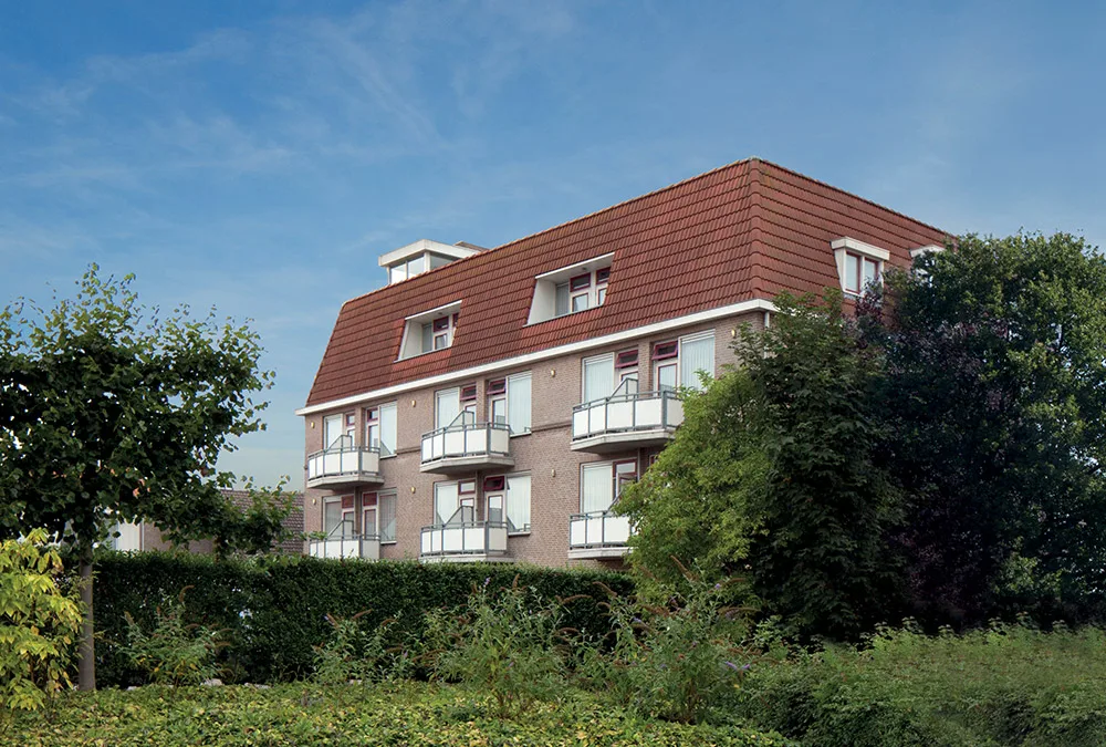 Representative hotel space: A multi-story residential building with a red roof stands behind landscaped greenery.