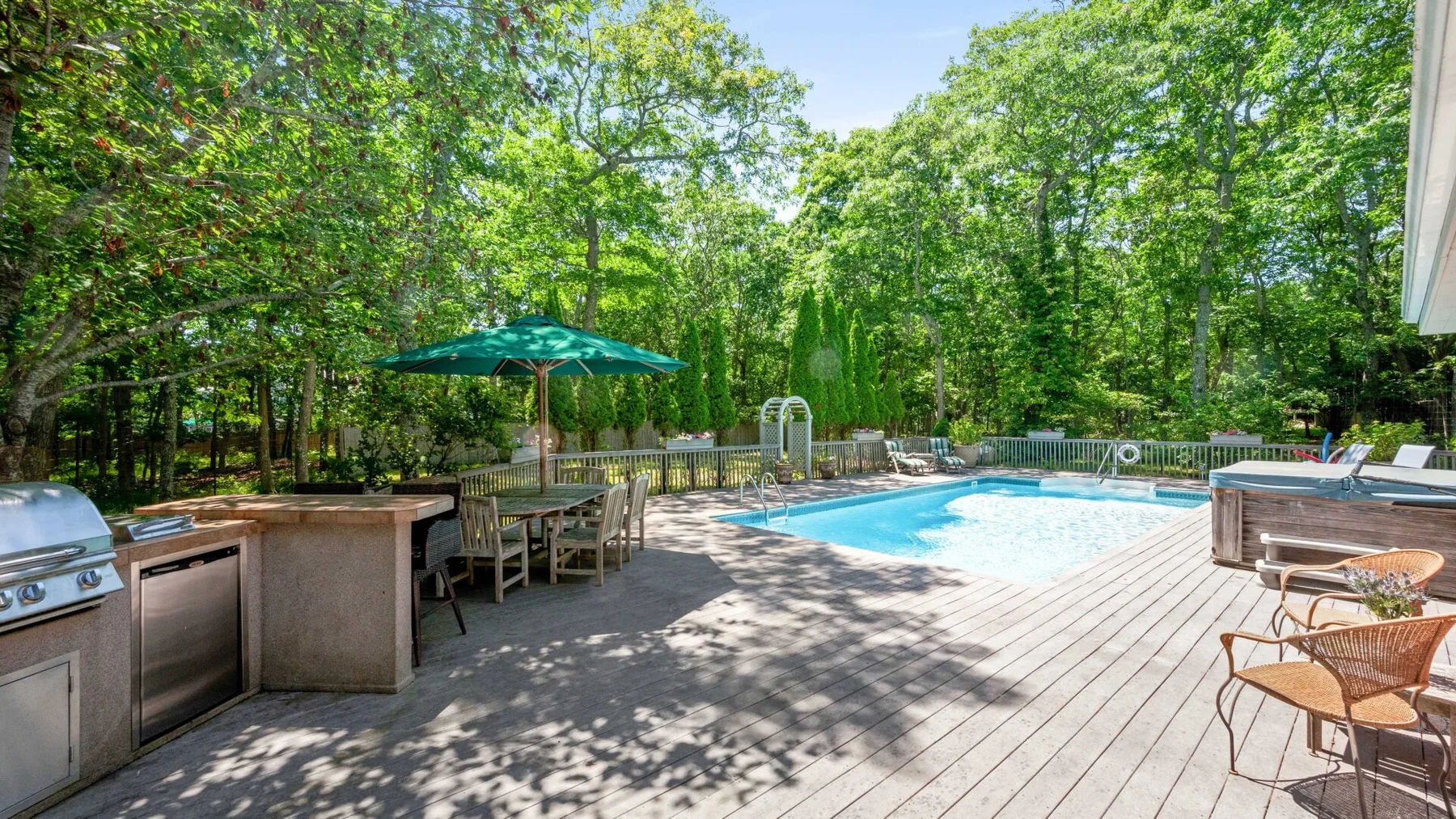 An outdoor pool area with a dining table and seating on a wooden deck.