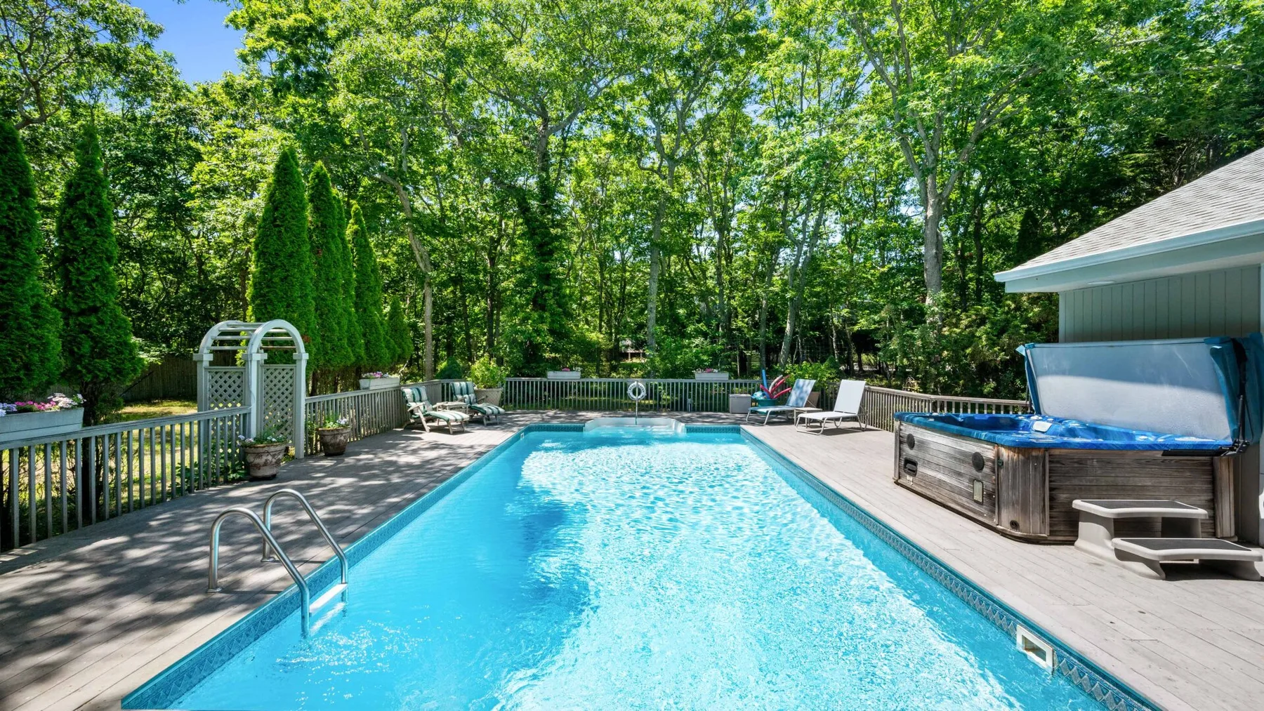 A backyard swimming pool sits beside a deck and a hot tub.