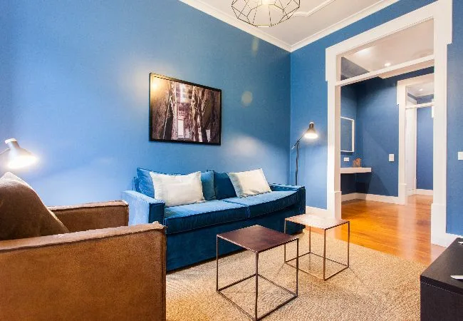 Una sala azul tiene un sofá, un sillón y dos mesitas.