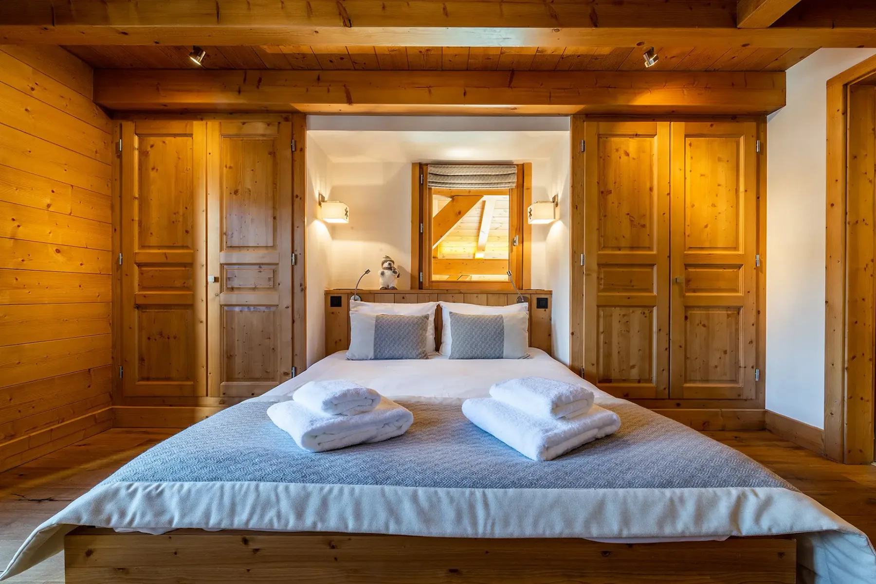 Un dormitorio con una cama doble, toallas dobladas y paneles de madera cálida.