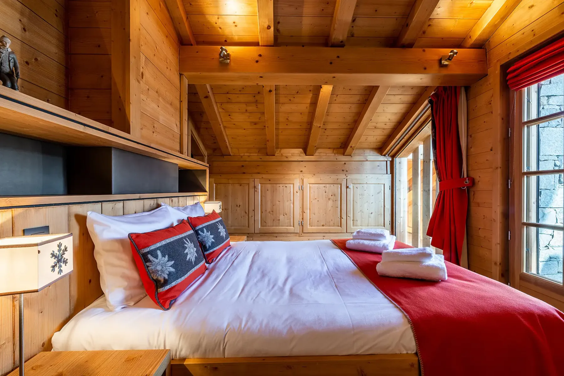 Un dormitorio con una cama, ropa de cama roja y paredes revestidas de madera.
