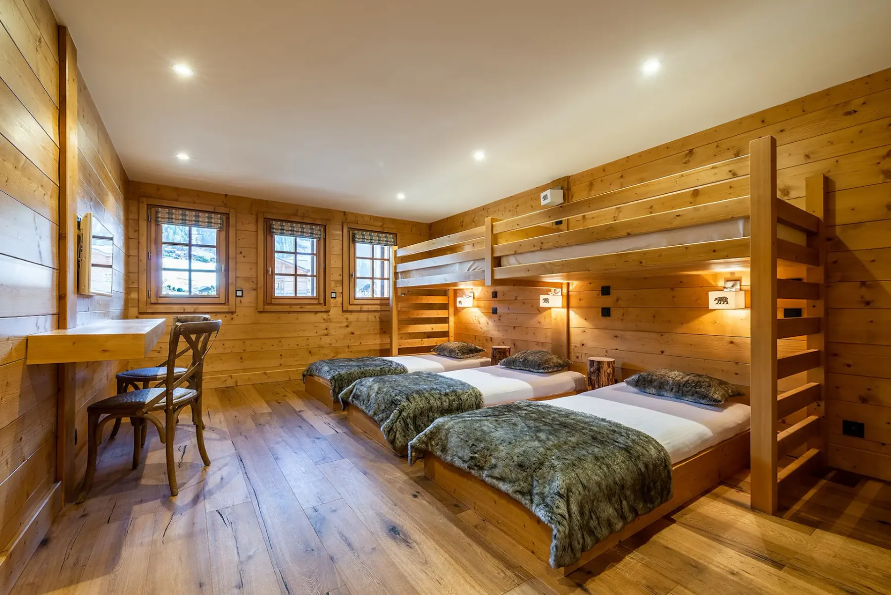 Un dormitorio revestido de madera con varias camas y ventanas a lo largo de una pared.