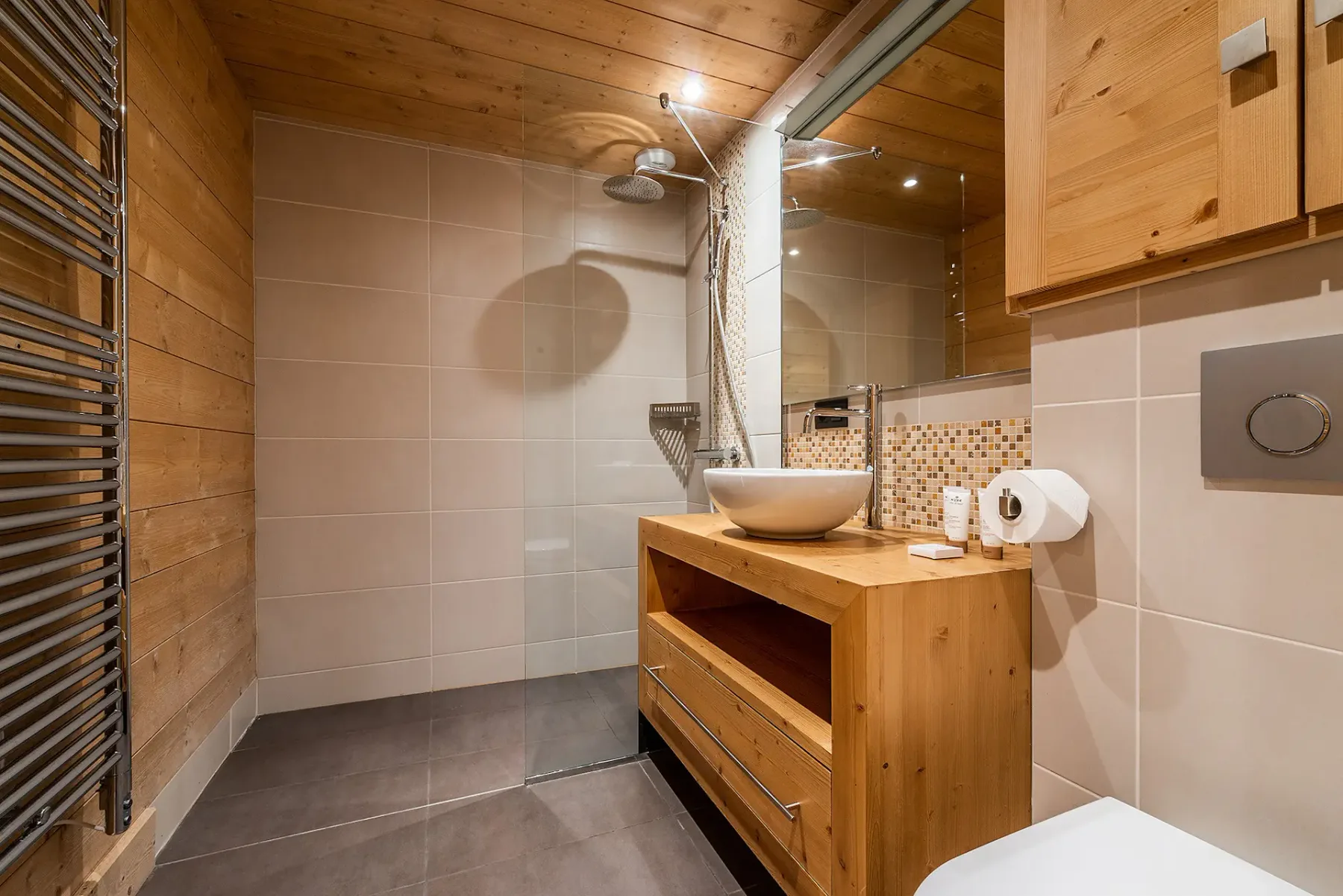 Un baño alicatado con un mueble de madera y una ducha mural.