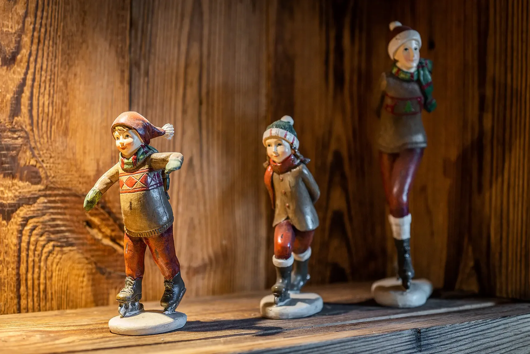 Pequeñas figuras pintadas están sobre un estante de madera frente a un fondo de paneles de madera.
