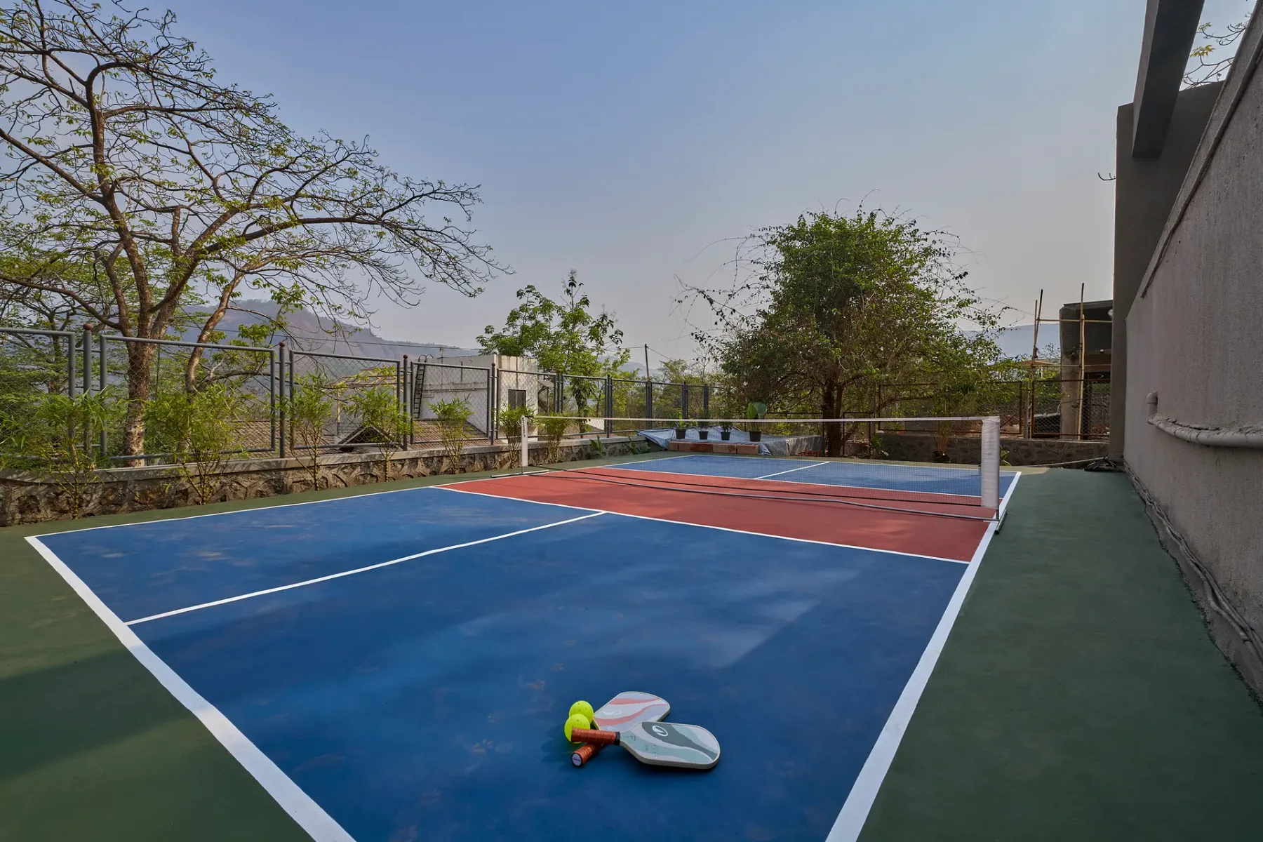 Una cancha exterior azul y roja tiene una red y paletas en el suelo.