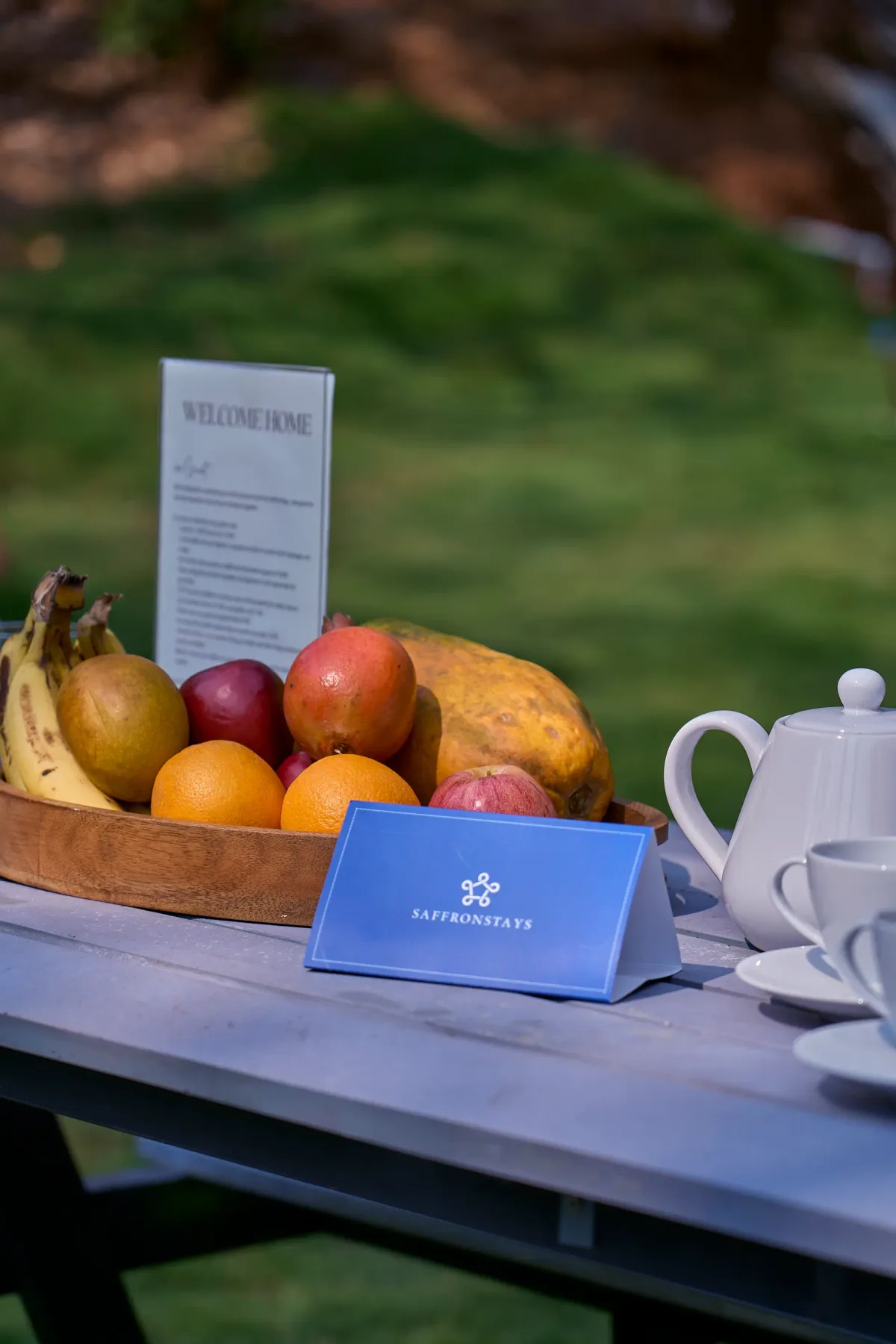 Una bandeja de frutas y un servicio de té están sobre una mesa exterior junto a un menú.