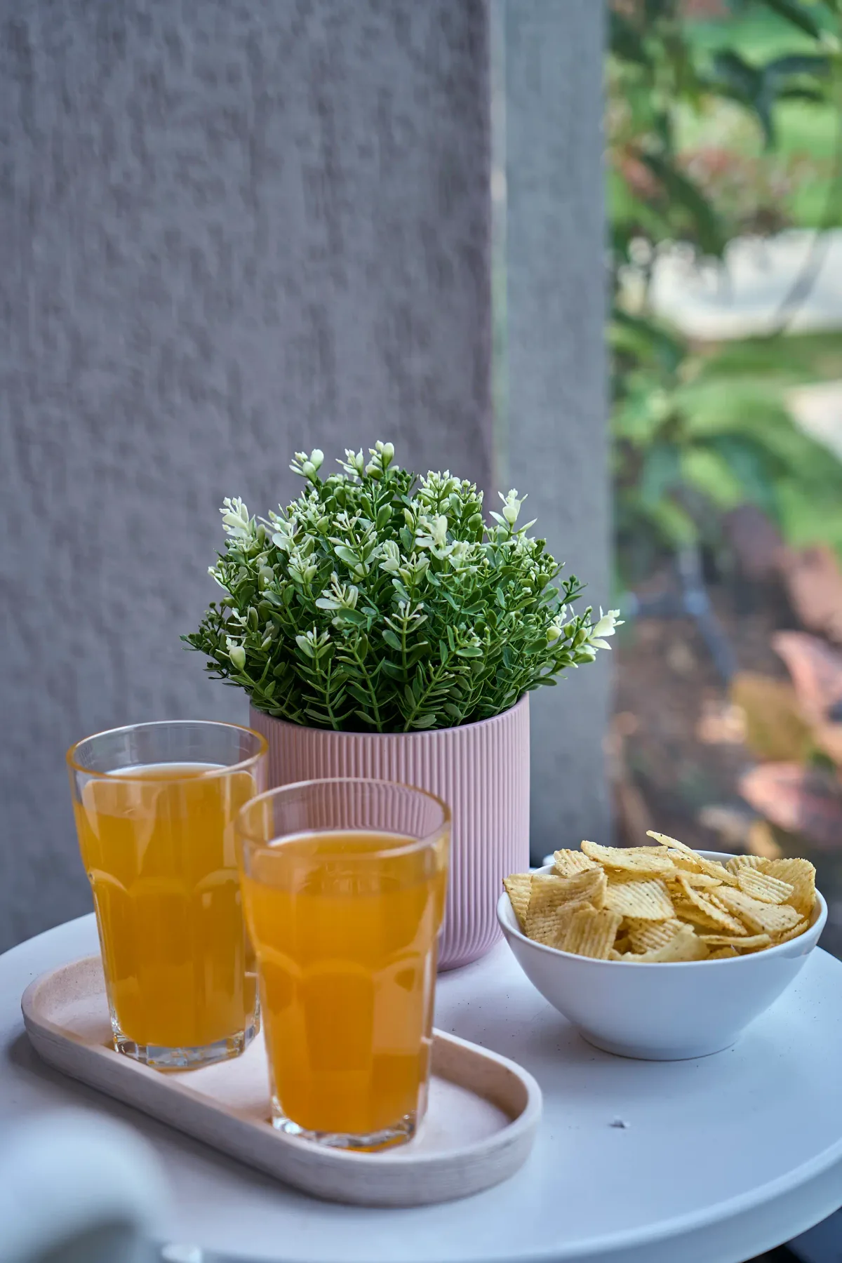 Una mesa pequeña sostiene dos vasos de bebida de naranja, un cuenco de patatas fritas y una planta en maceta.