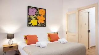 Un dormitorio con una cama bien tendida, almohadas coloridas y arte floral en la pared.