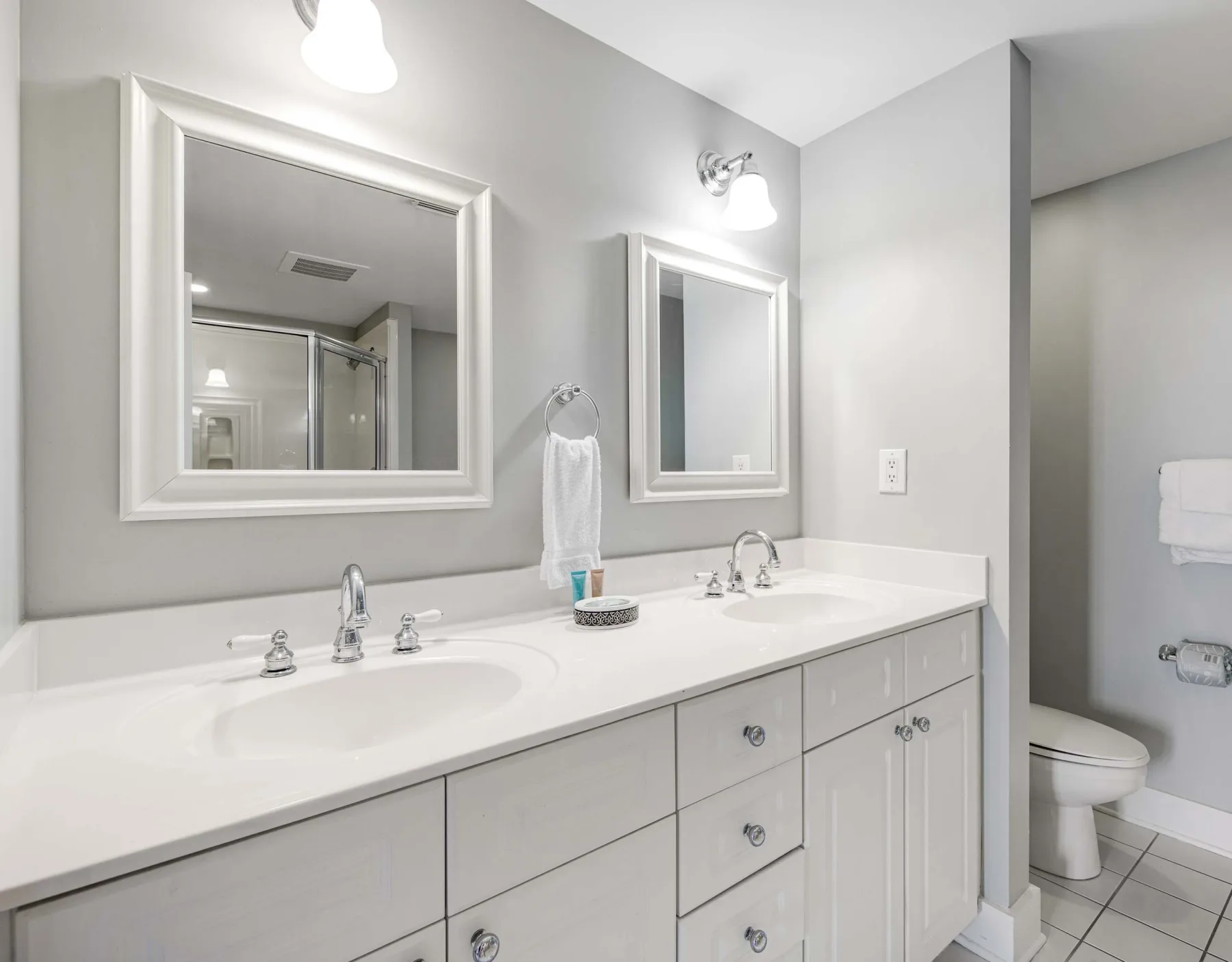 A bathroom vanity with a long white counter, sinks, mirrors, and a toilet.