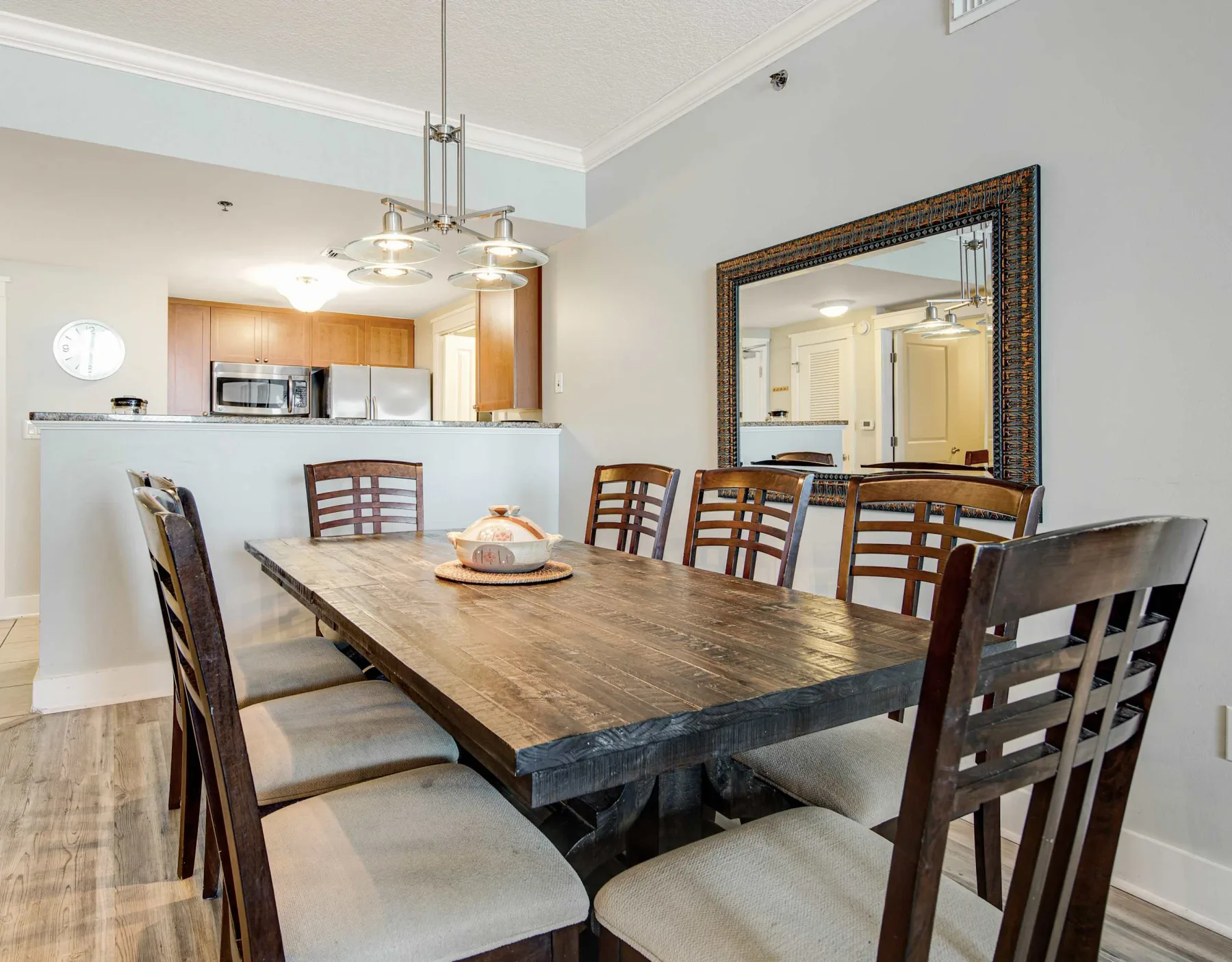 A dining area with a long wooden table and seating, beside an open kitchen.