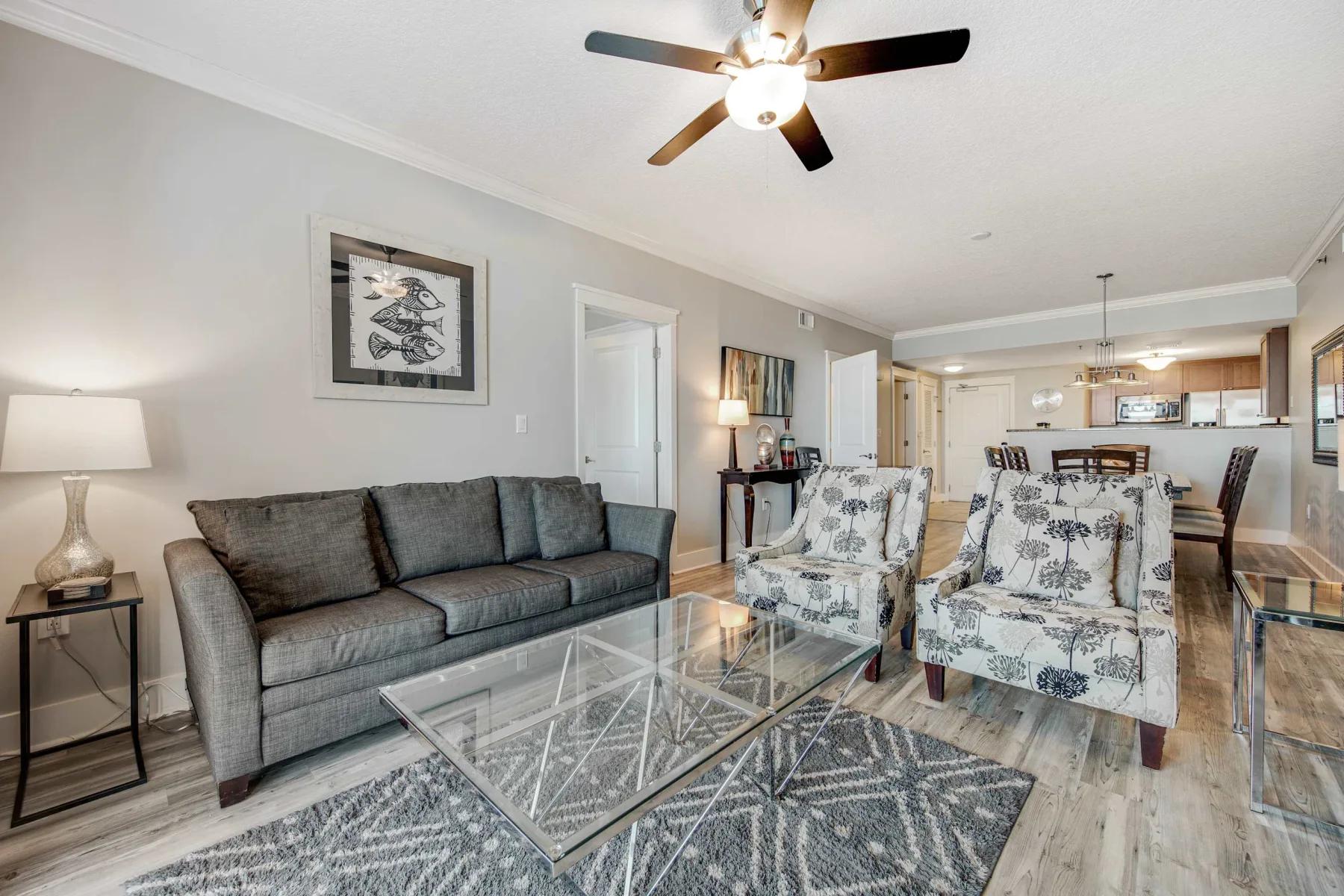 A living room with a gray sofa, patterned armchairs, and a glass coffee table.