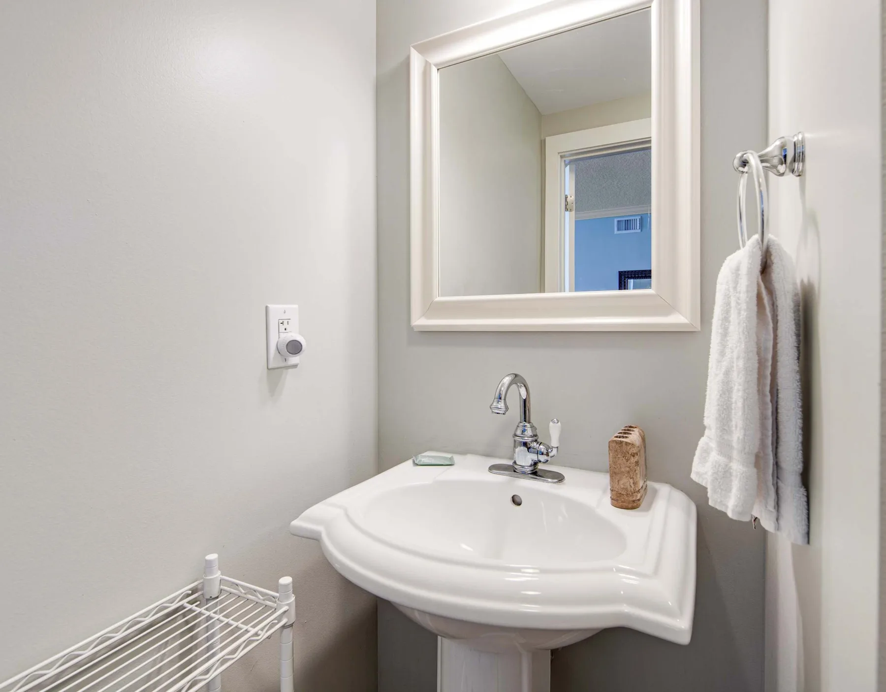 A bathroom sink sits beneath a mirror, with towels hanging beside it.
