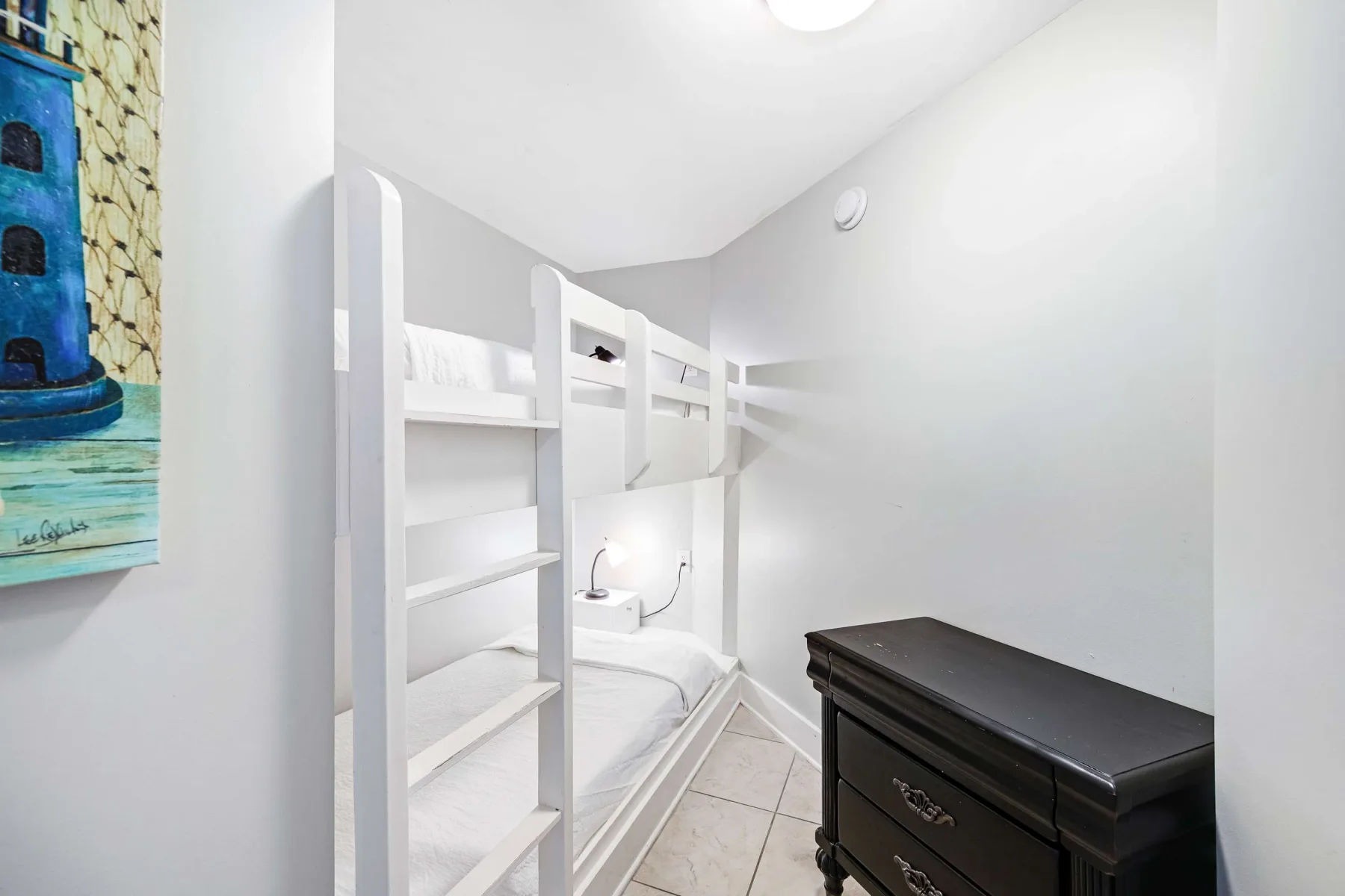 A compact bunk-bed sleeping area with white bedding and a dark dresser.