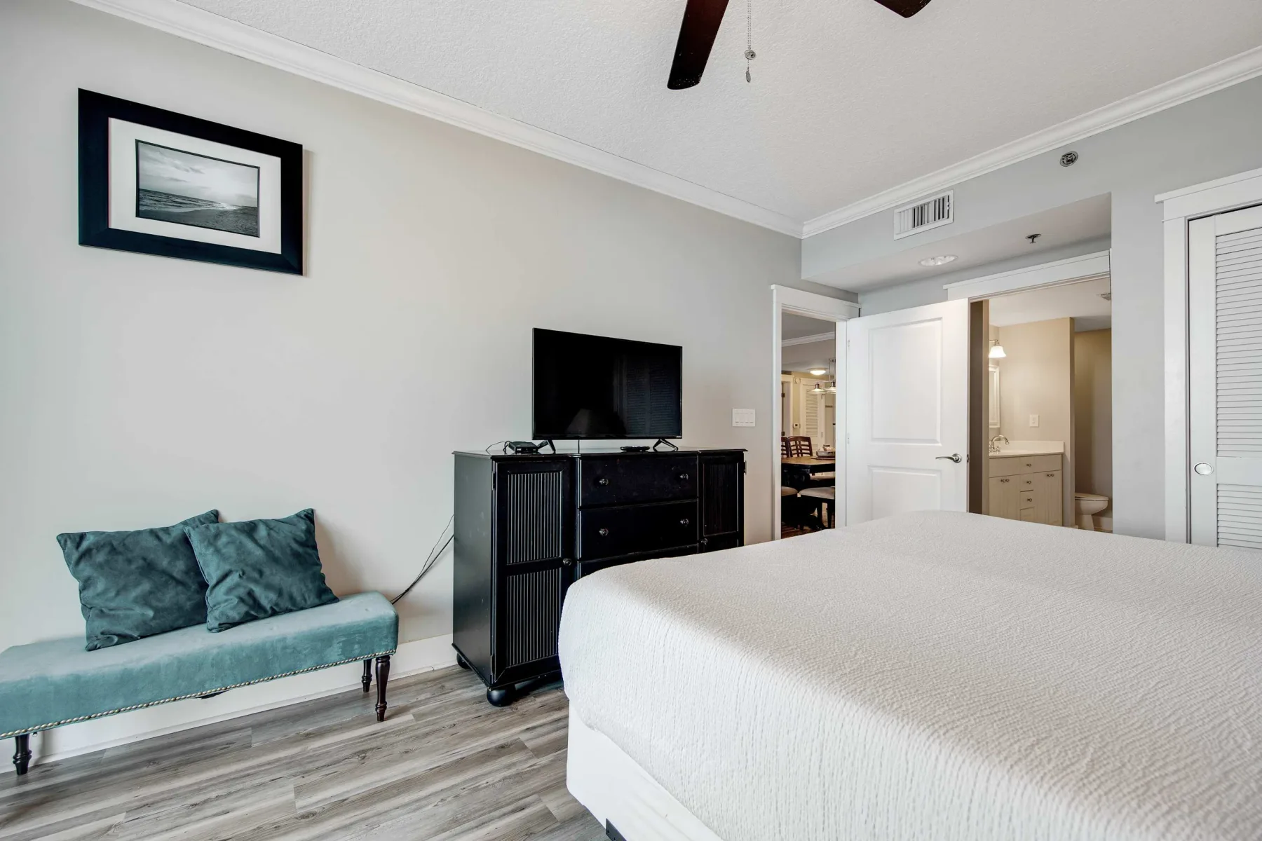 A bedroom with a bed, a television on a dresser, and a small upholstered bench.