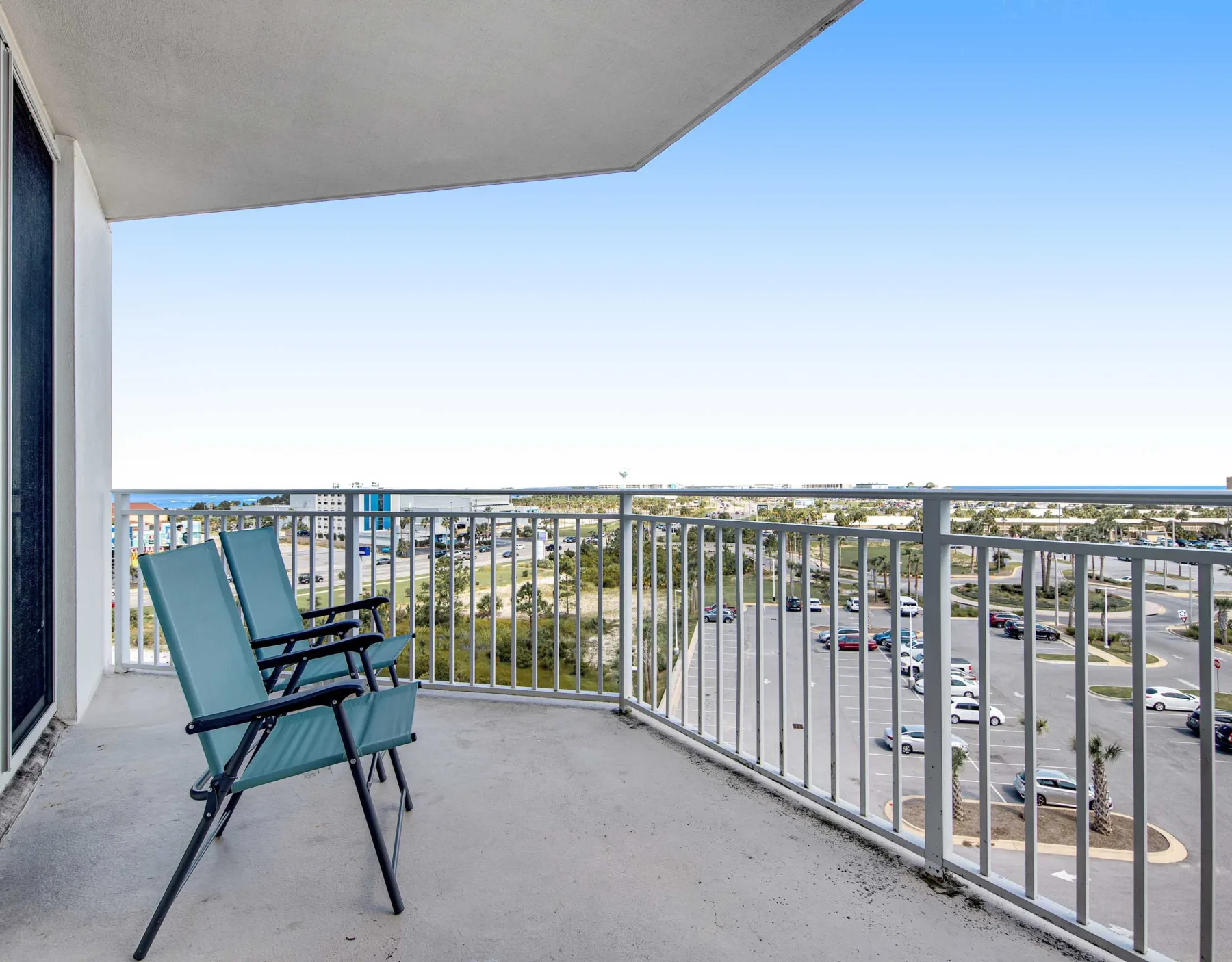 A balcony with seating overlooks a parking lot and nearby buildings.