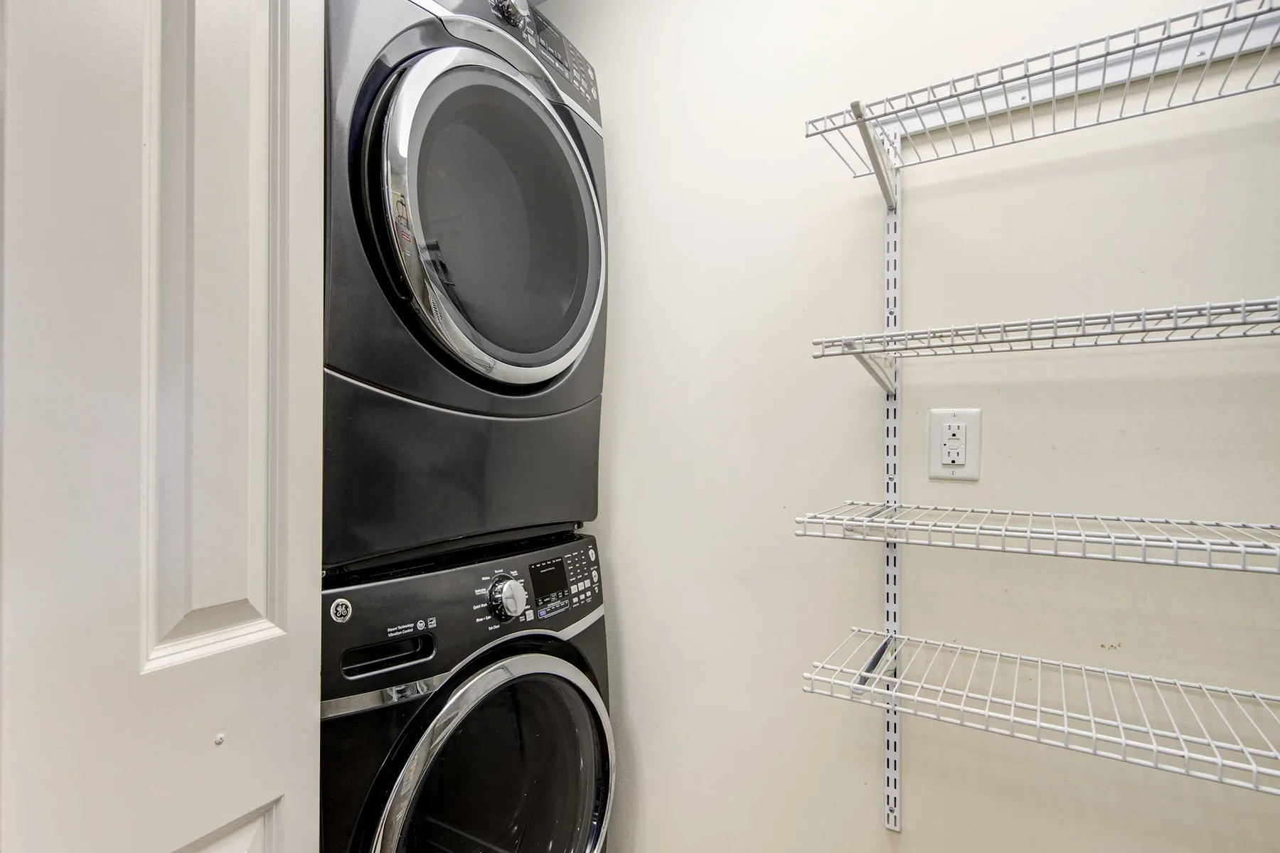 A laundry area with a stacked washer and dryer beside wire shelves.