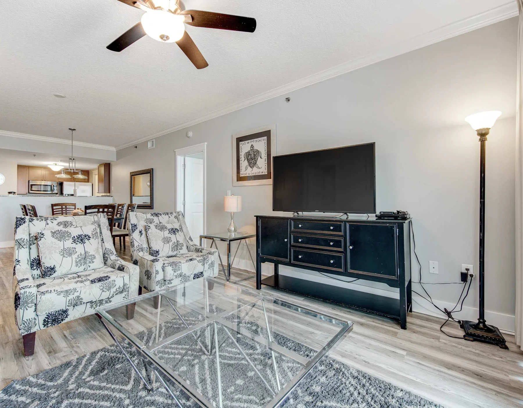 A living room with patterned seating, a glass coffee table, and a television.