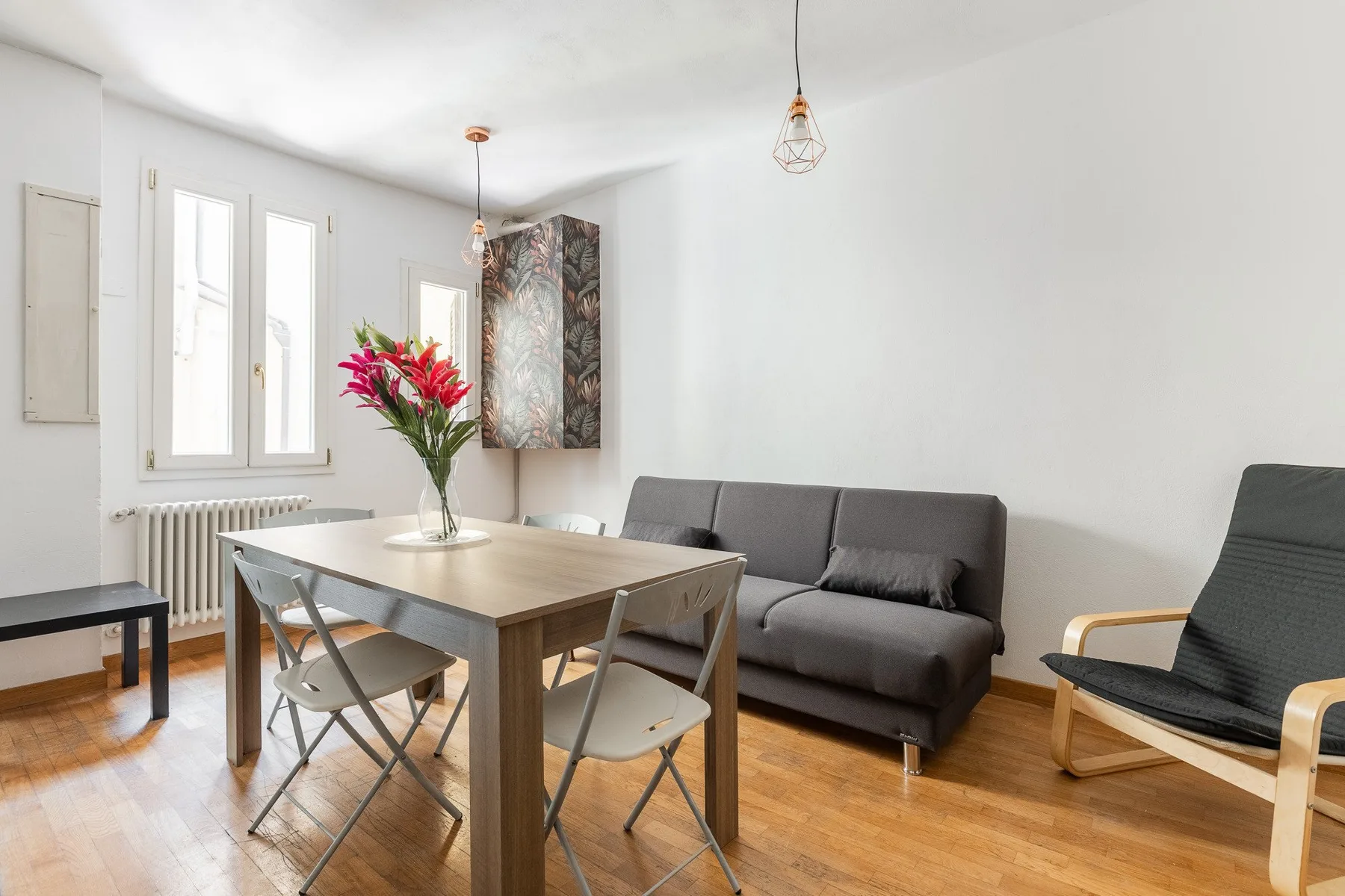 A bright living and dining area with a gray sofa and a wooden table.